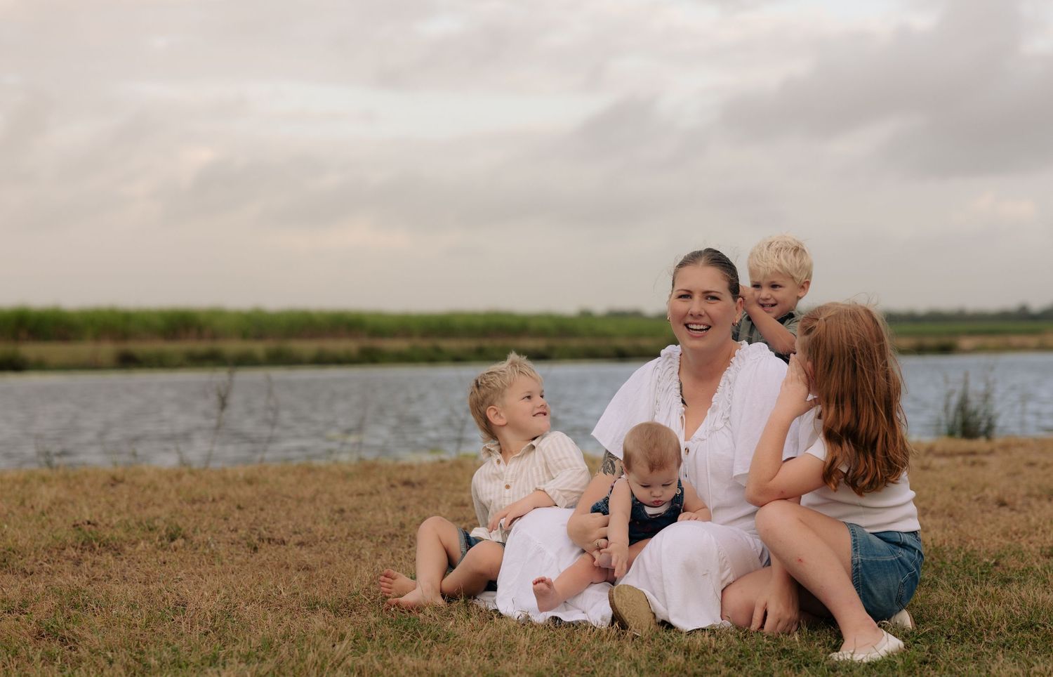 A family sits together on grassy ground near a lake during golden hour.