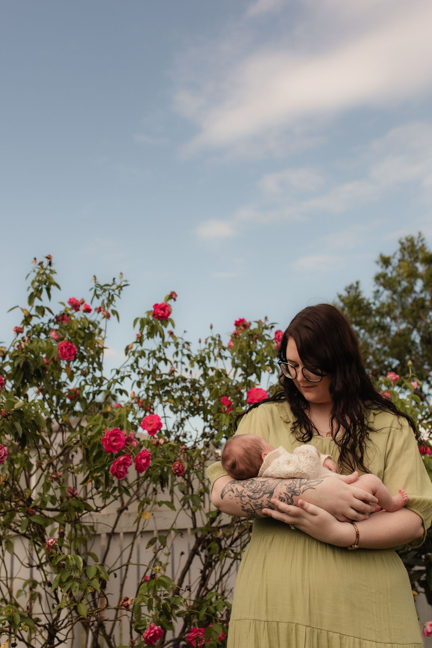 A tender moment between parent and newborn by blooming red roses in a garden setting.