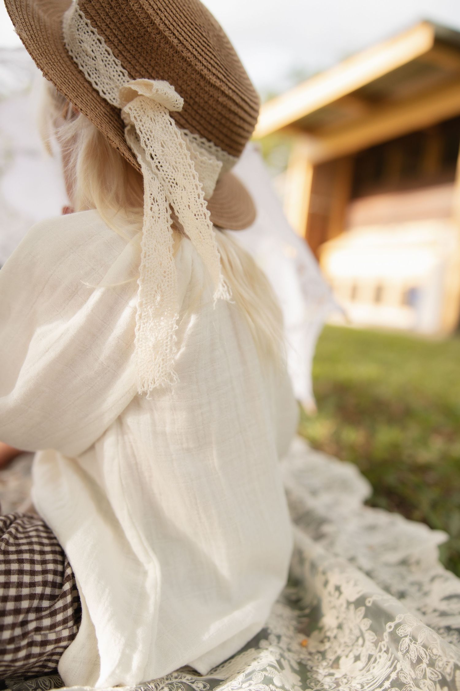 Close-up view of a straw hat with lace trim and white dress in sunlit outdoor setting.