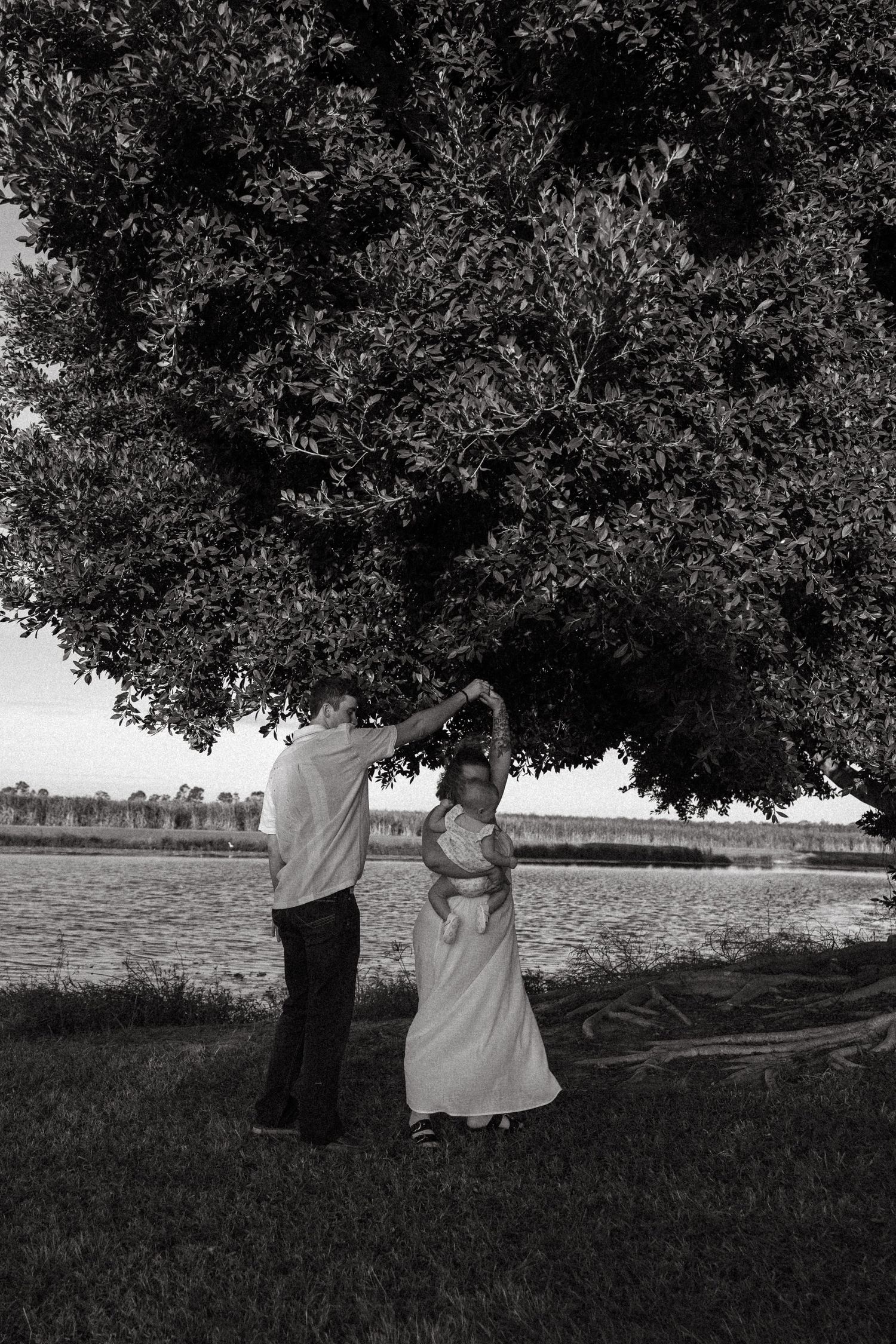 A couple dancing under a large tree in black and white photography.