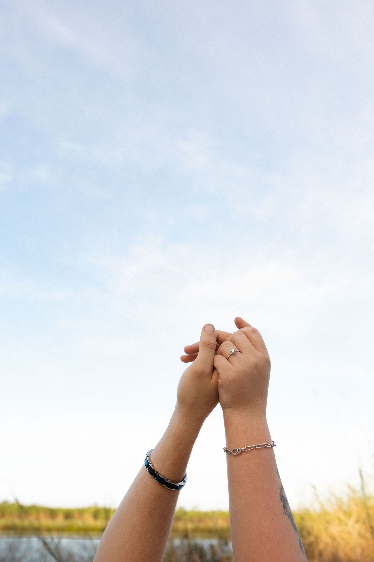 Two hands clasped together against a bright blue sky with bracelets visible on the wrists.