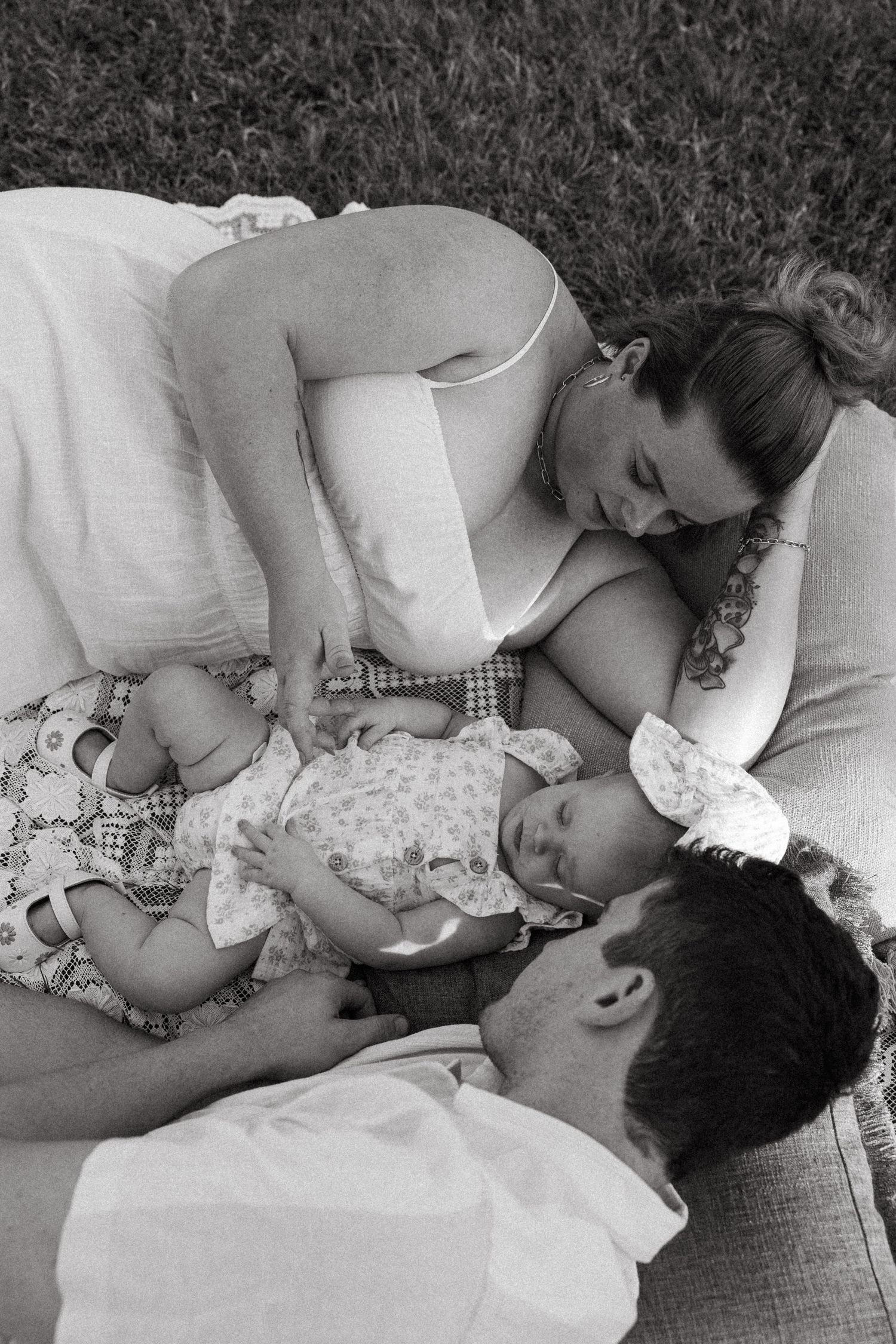 A black and white photo of a family resting together on a blanket outdoors.
