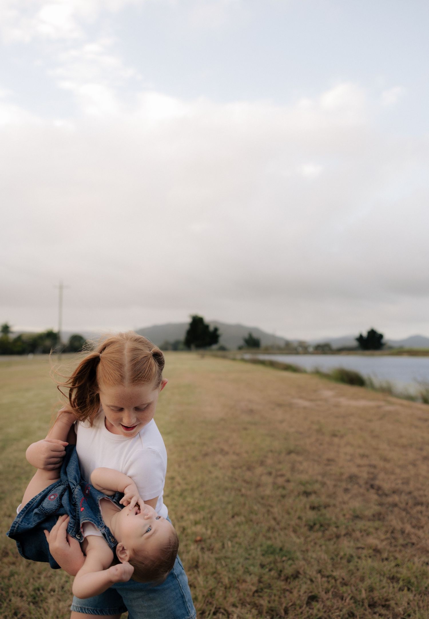 Two people sharing a playful moment on a grassy hillside by the water.