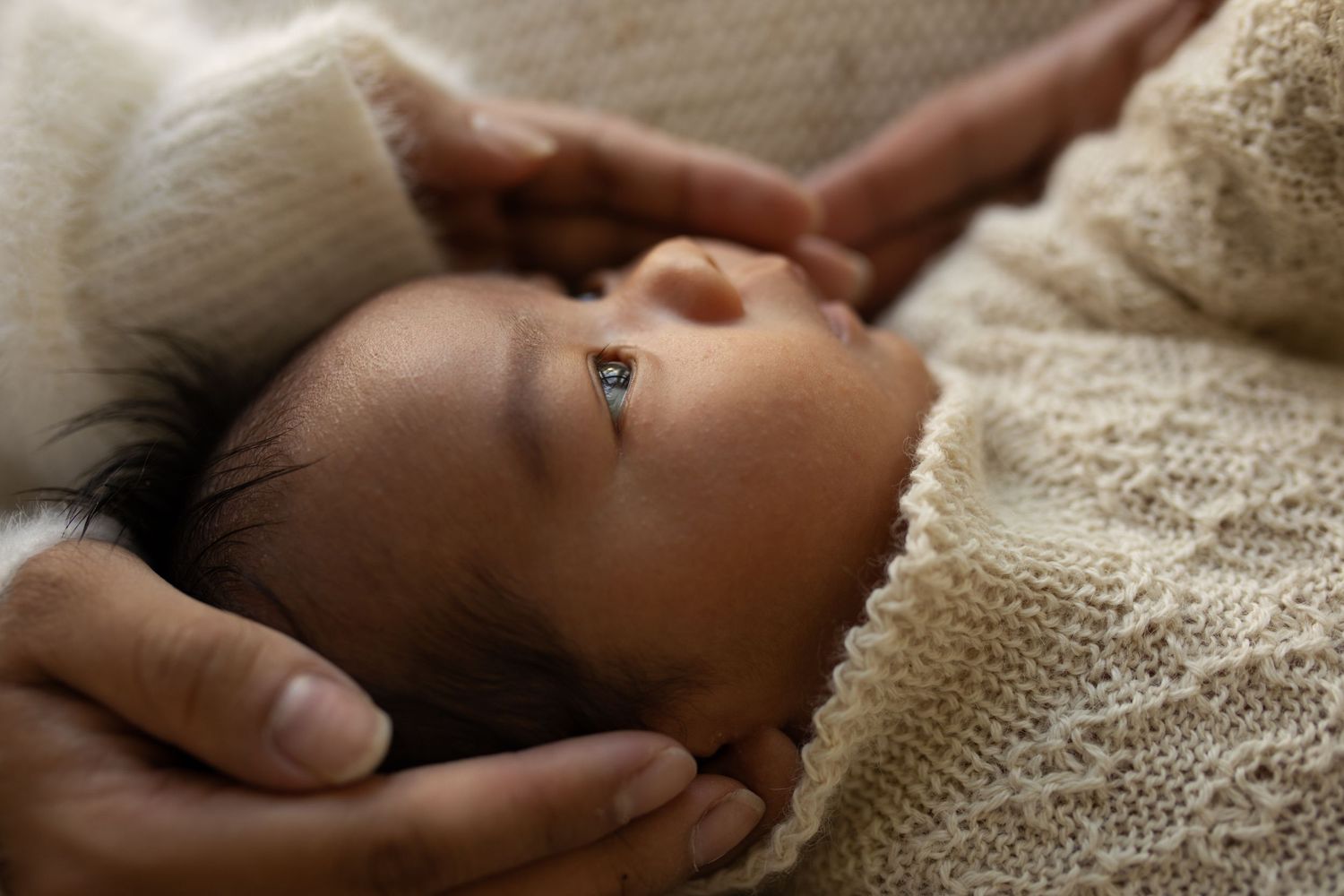 A small baby lies on cream bedding as gentle hands cradle their head.