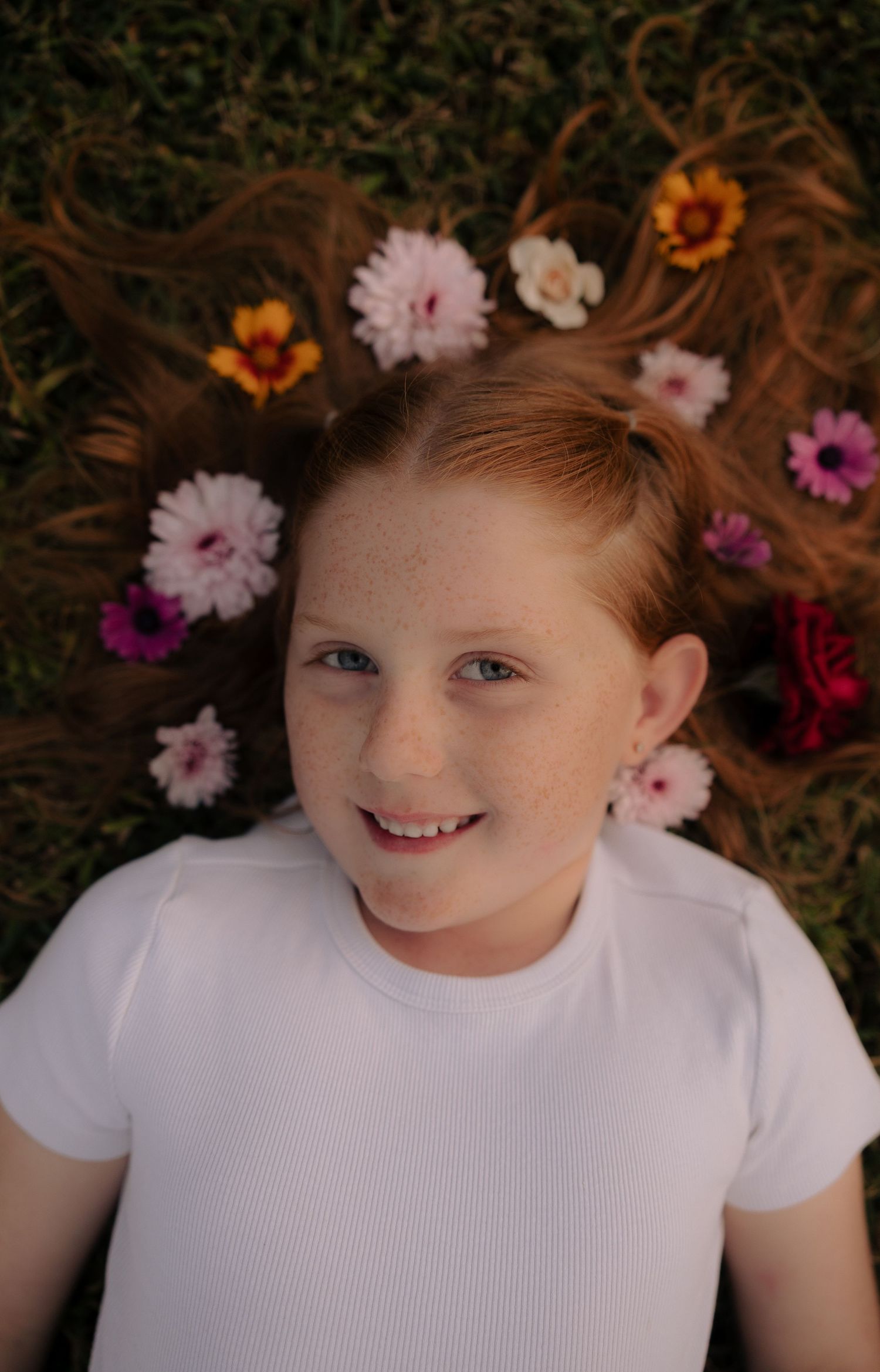 Close-up portrait of a child surrounded by pink and orange flowers in their hair.