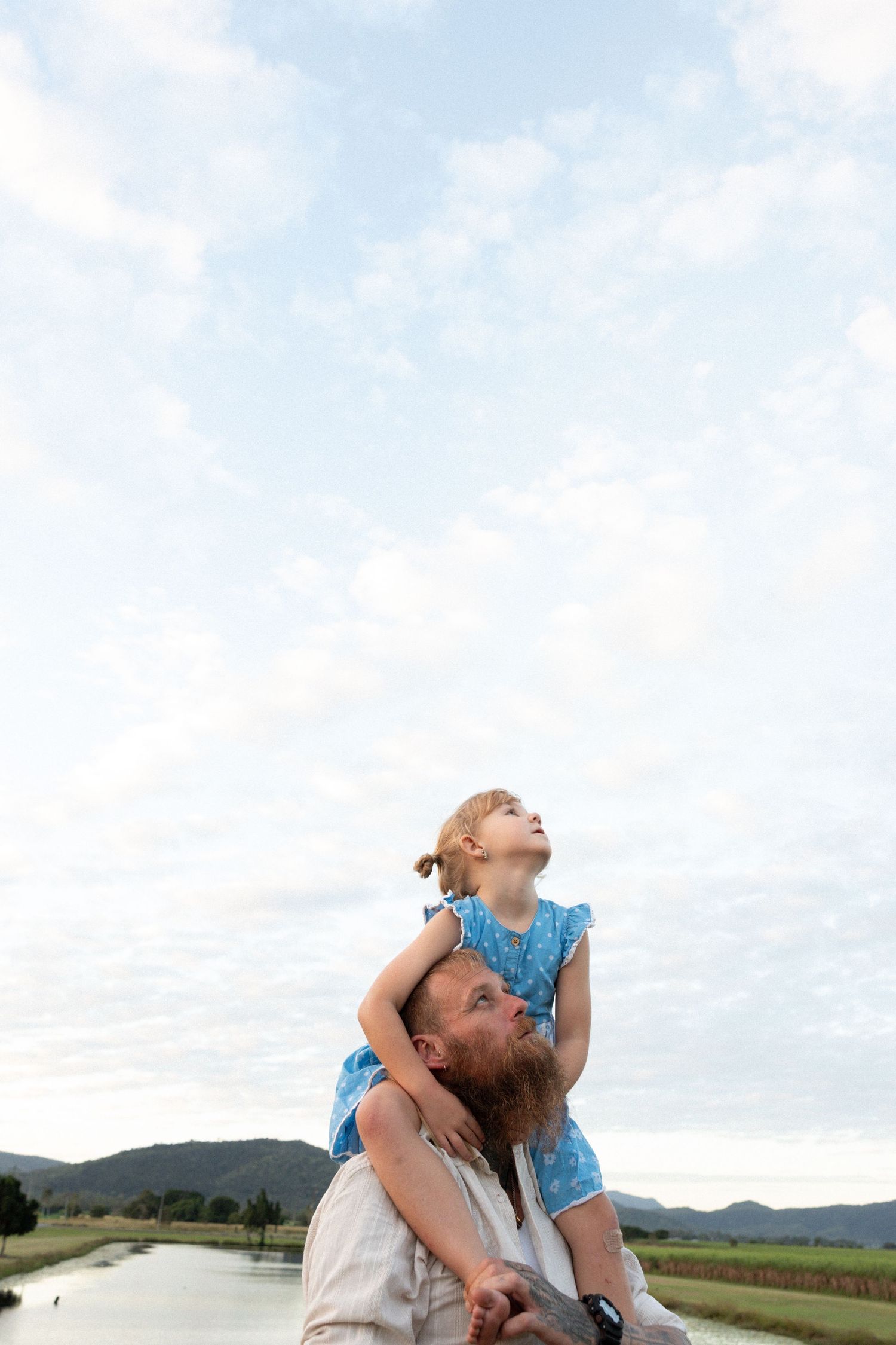 A child riding on someone's shoulders against a cloudy sky with mountains in the background.