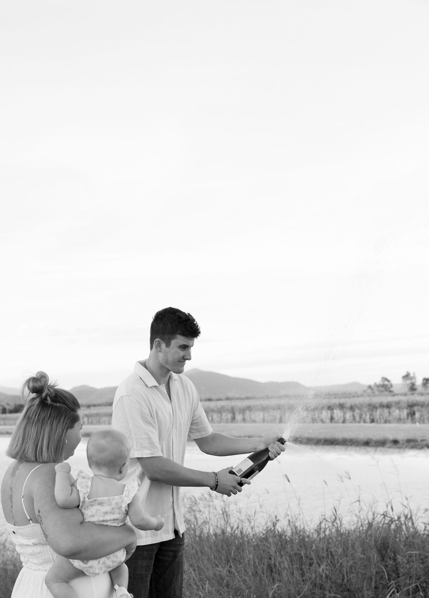 A couple sharing a moment by a lake while holding what appears to be a champagne bottle.
