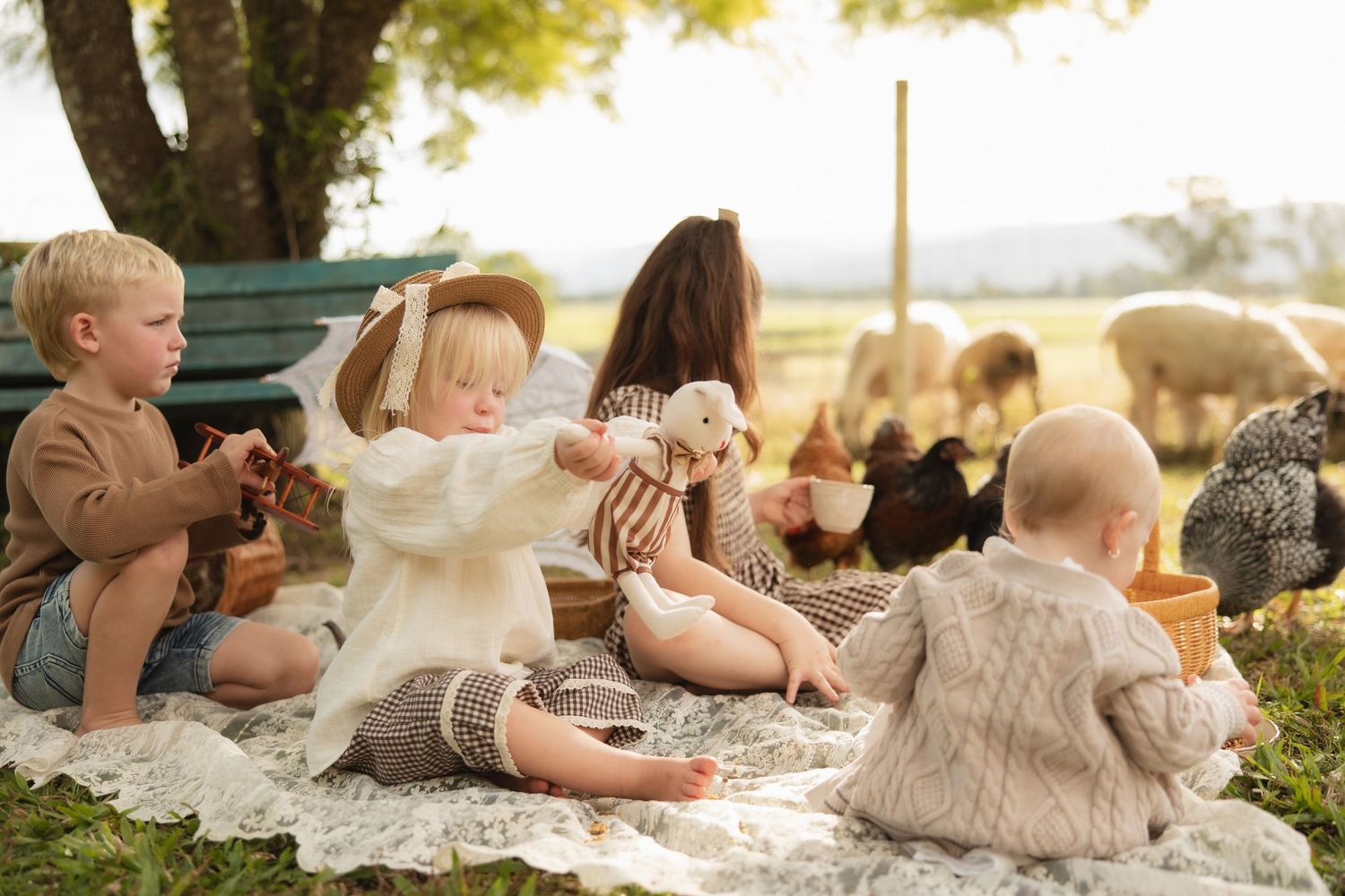 Children enjoying a picnic outdoors on a blanket while chickens roam in the golden afternoon sunlight.