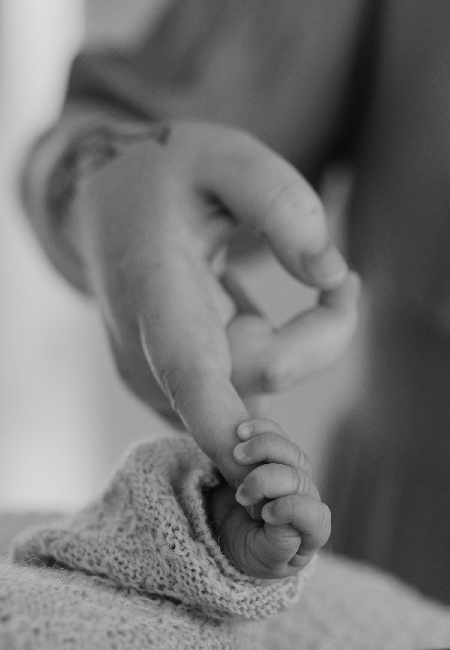 Close-up black and white photo of a baby's tiny foot wrapped in a knit blanket.