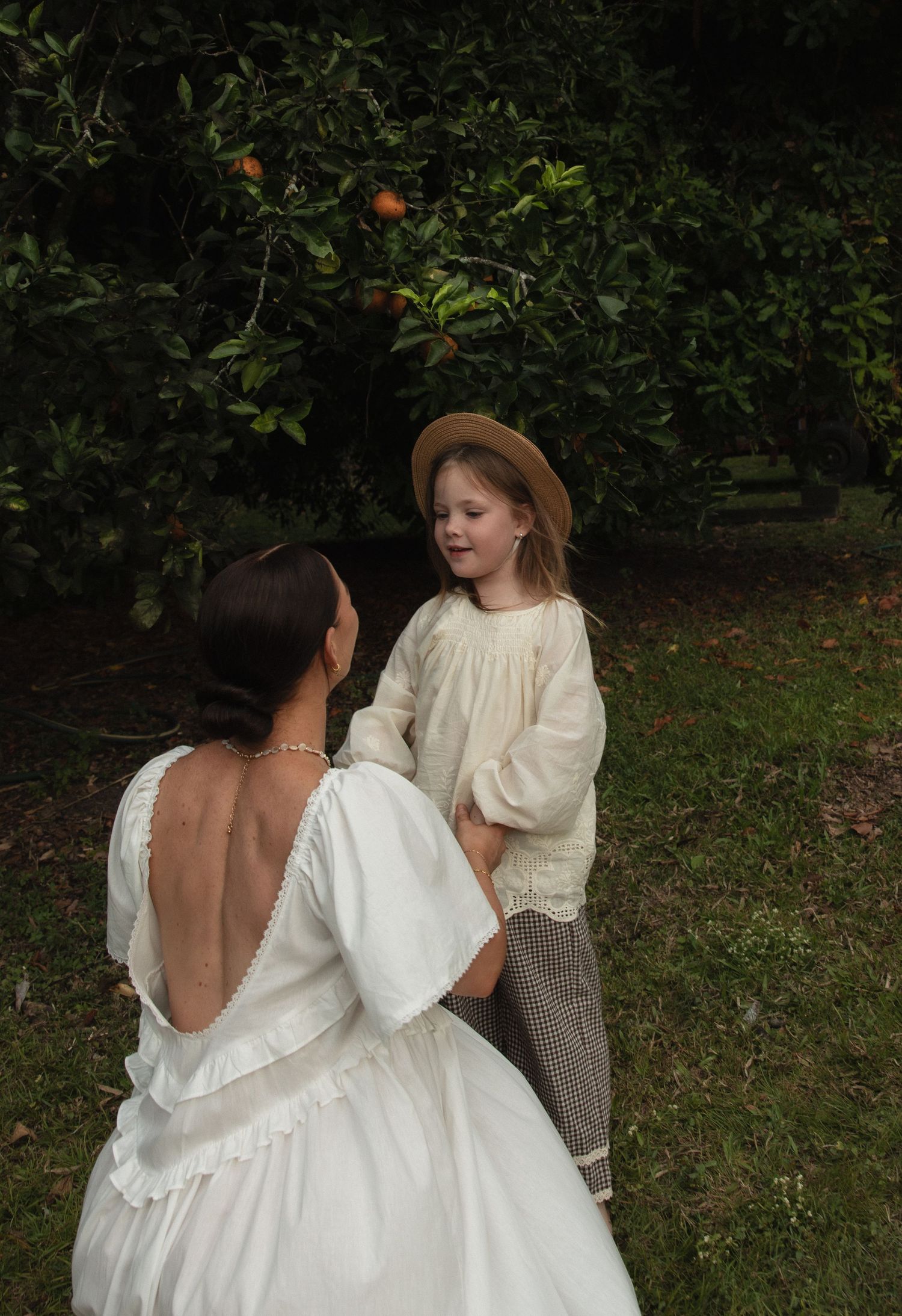 A pastoral scene in an apple orchard featuring two individuals in white vintage-style dresses among the trees.