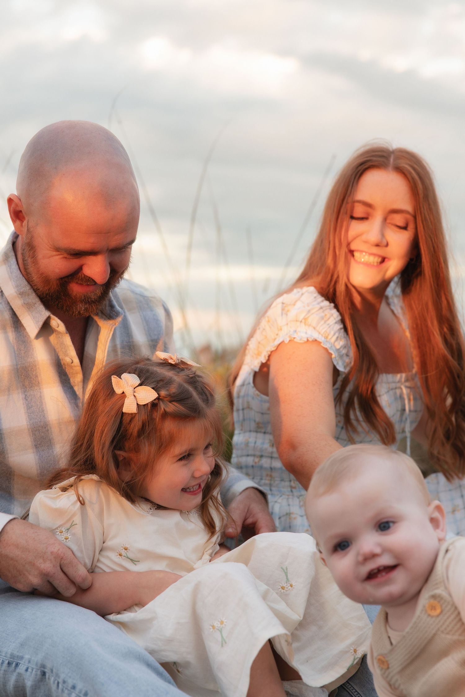 In a dreamy outdoor setting at sunset, a small family shares tender moments together in matching cream-colored outfits.
