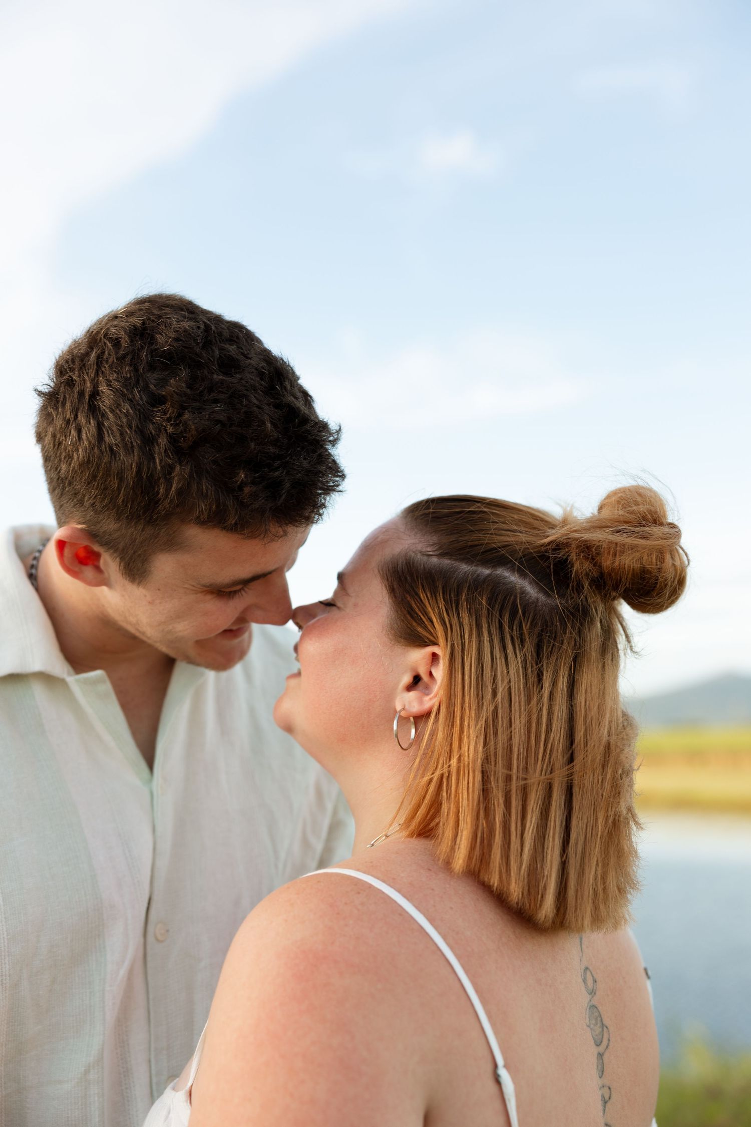 Romantic close up of couple sharing an intimate moment against blue sky and water.