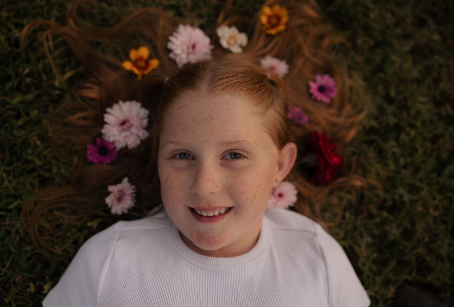 A portrait of a child lying on grass surrounded by colorful flowers.