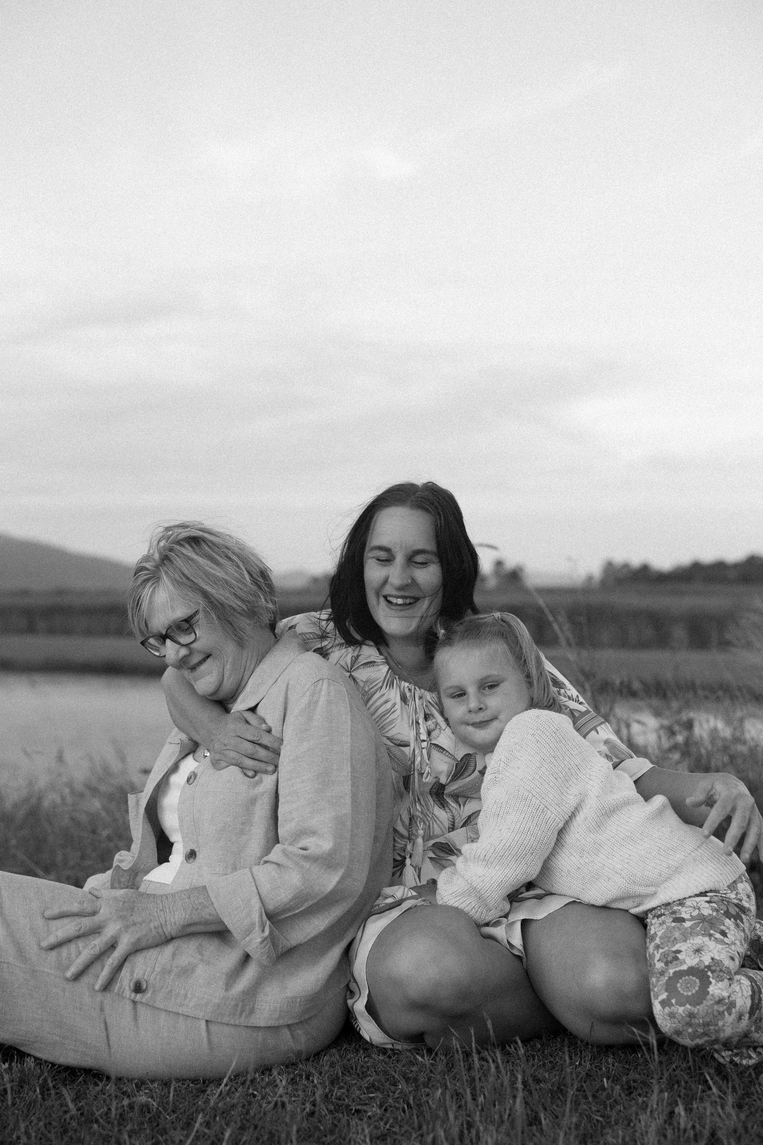 Black and white portrait of three generations sharing warm embrace by the lake.