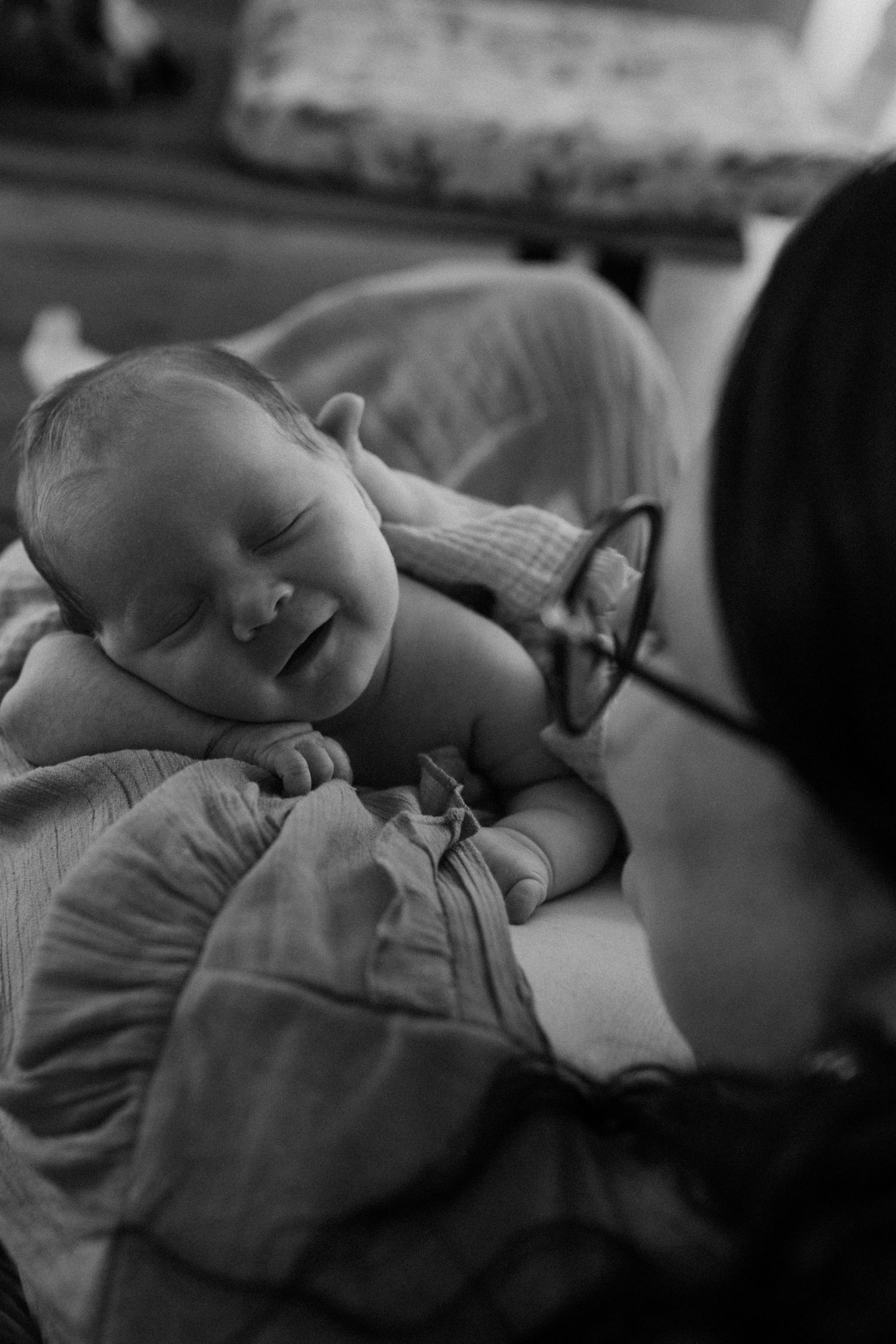 A black and white portrait of a smiling sleeping baby being watched by their parent.