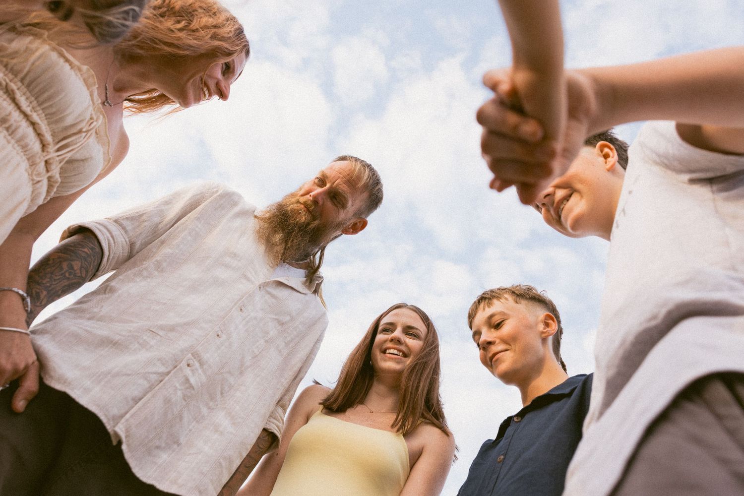 A low-angle view of a group of people standing in a circle on a sunny day looking down at the camera.