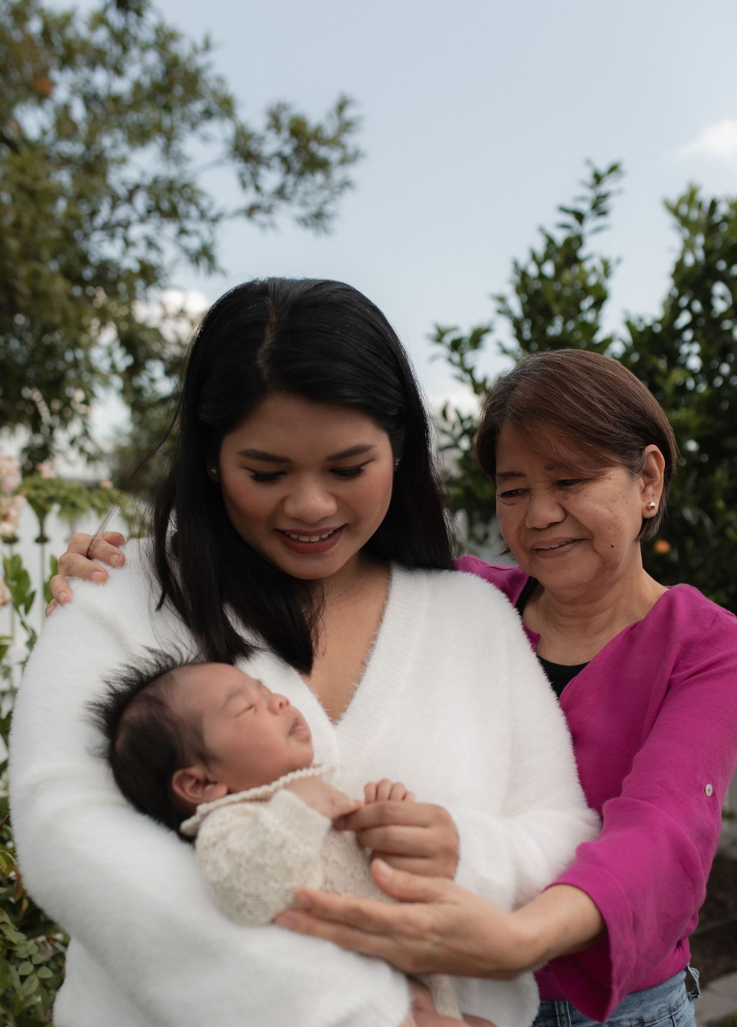 A tender outdoor family moment with a sleeping newborn wearing white lace being held lovingly.