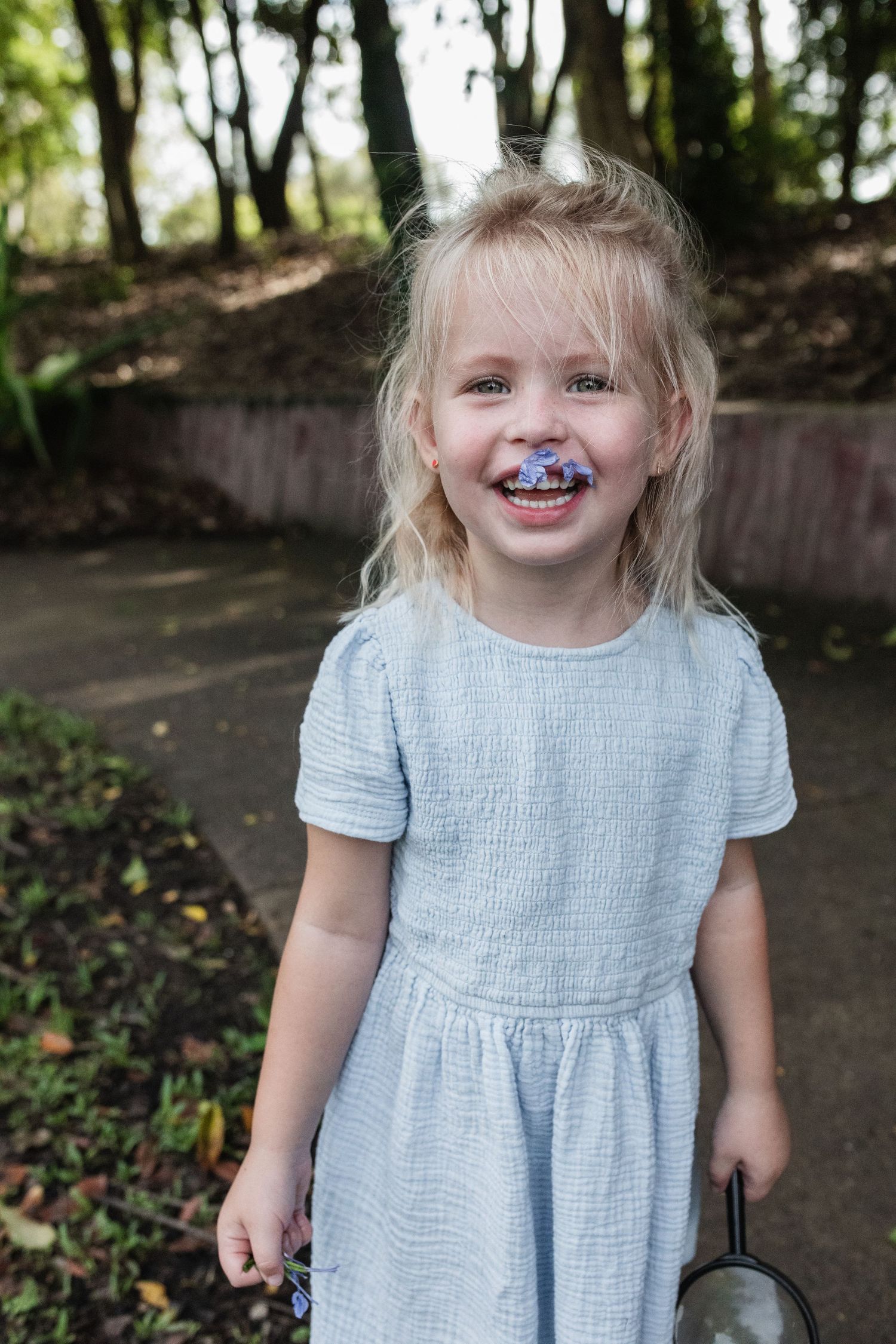 Child in light blue dress with colorful stains around mouth smiling outdoors.