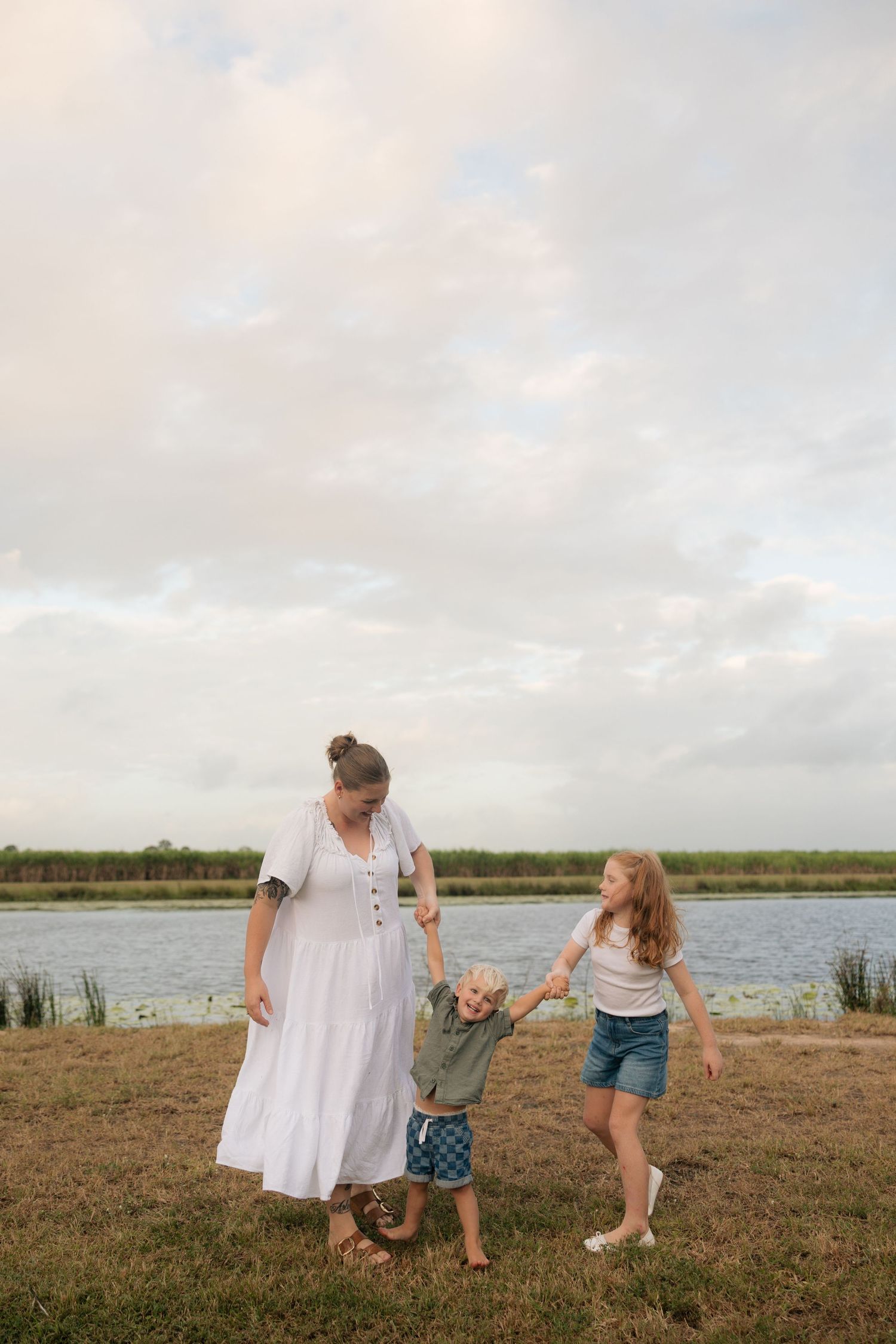 Family enjoying a peaceful moment by the lake at sunset, standing together on grassy shoreline.