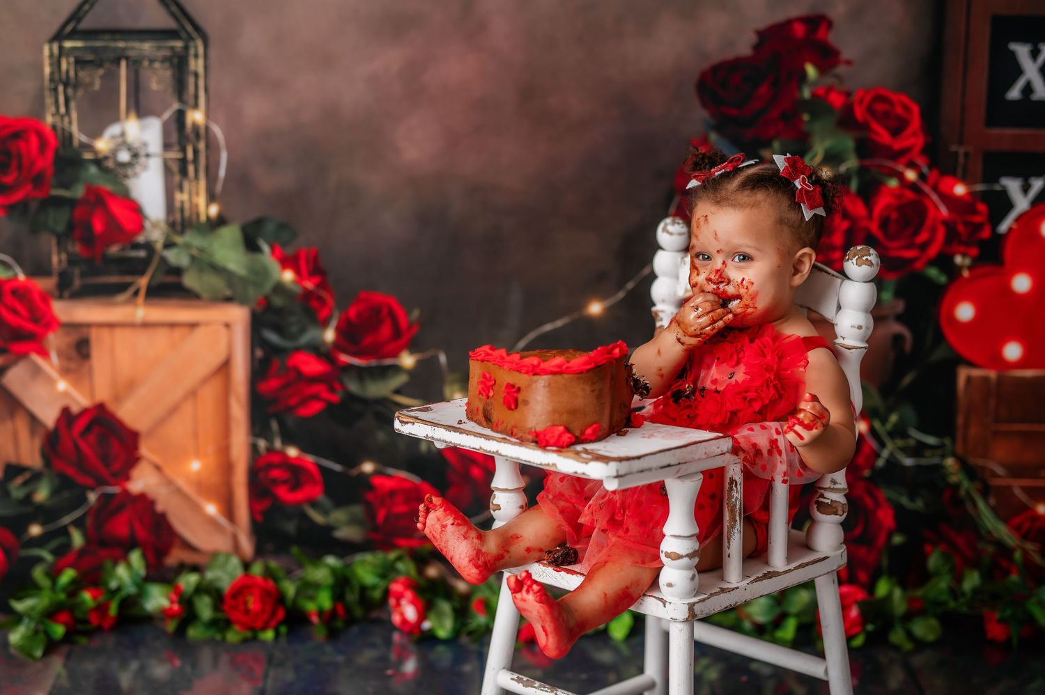 Small child in red tulle dress seated among romantic Valentine's day decor with roses.