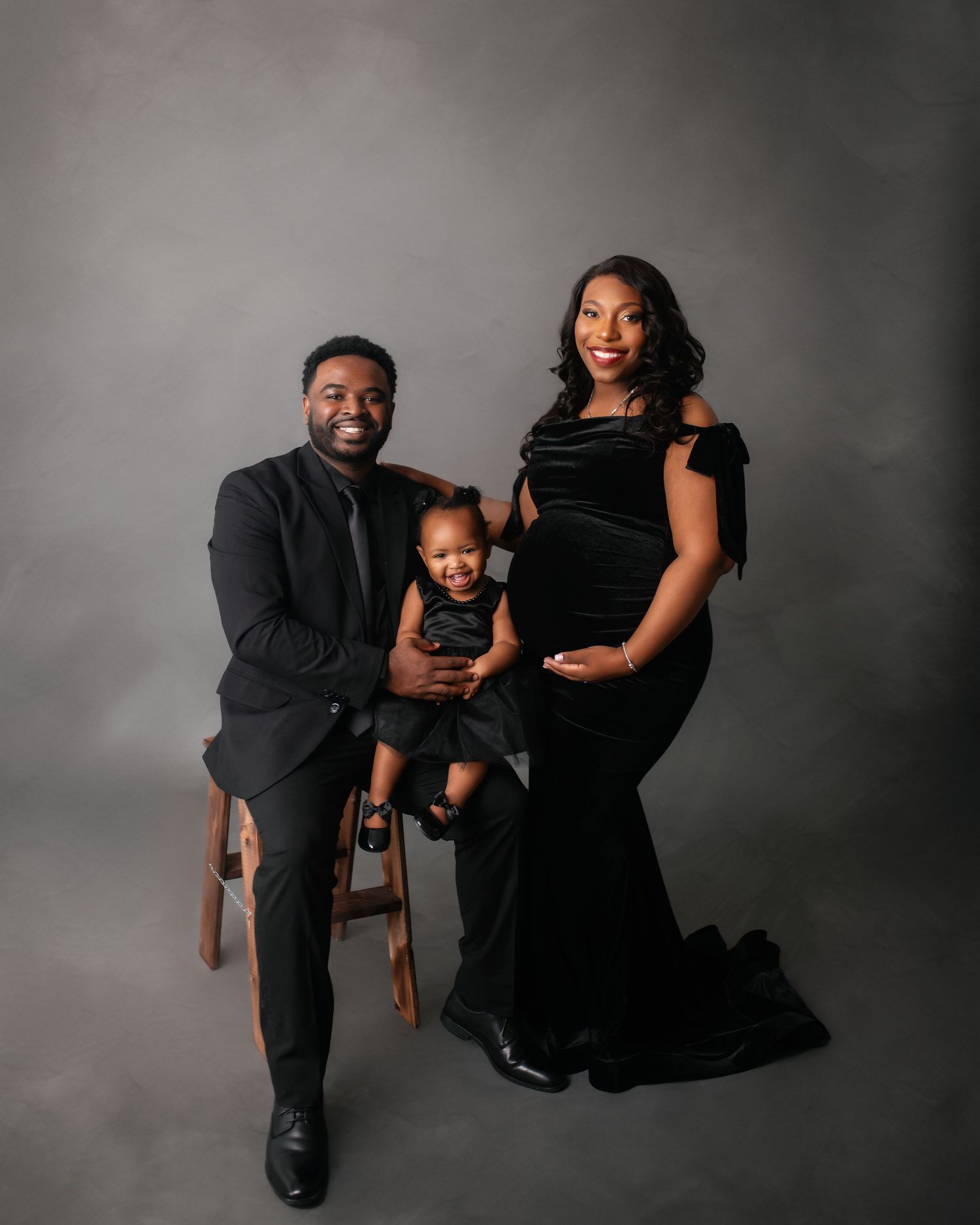 Formal family portrait with toddler in black attire against grey backdrop.
