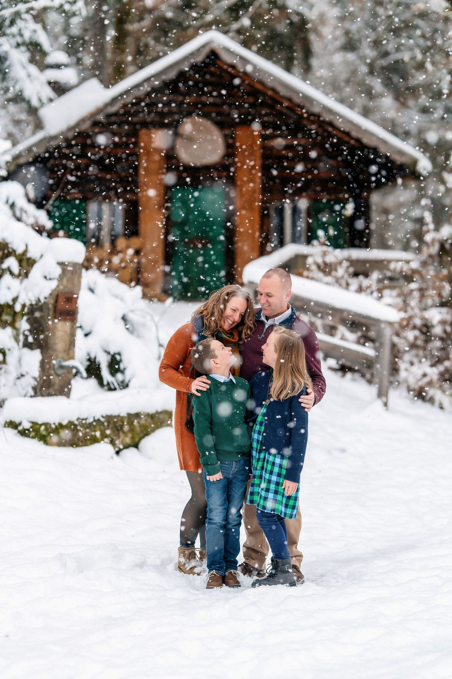 A family shares a joyful moment in the snow outside a rustic cabin with falling snowflakes.