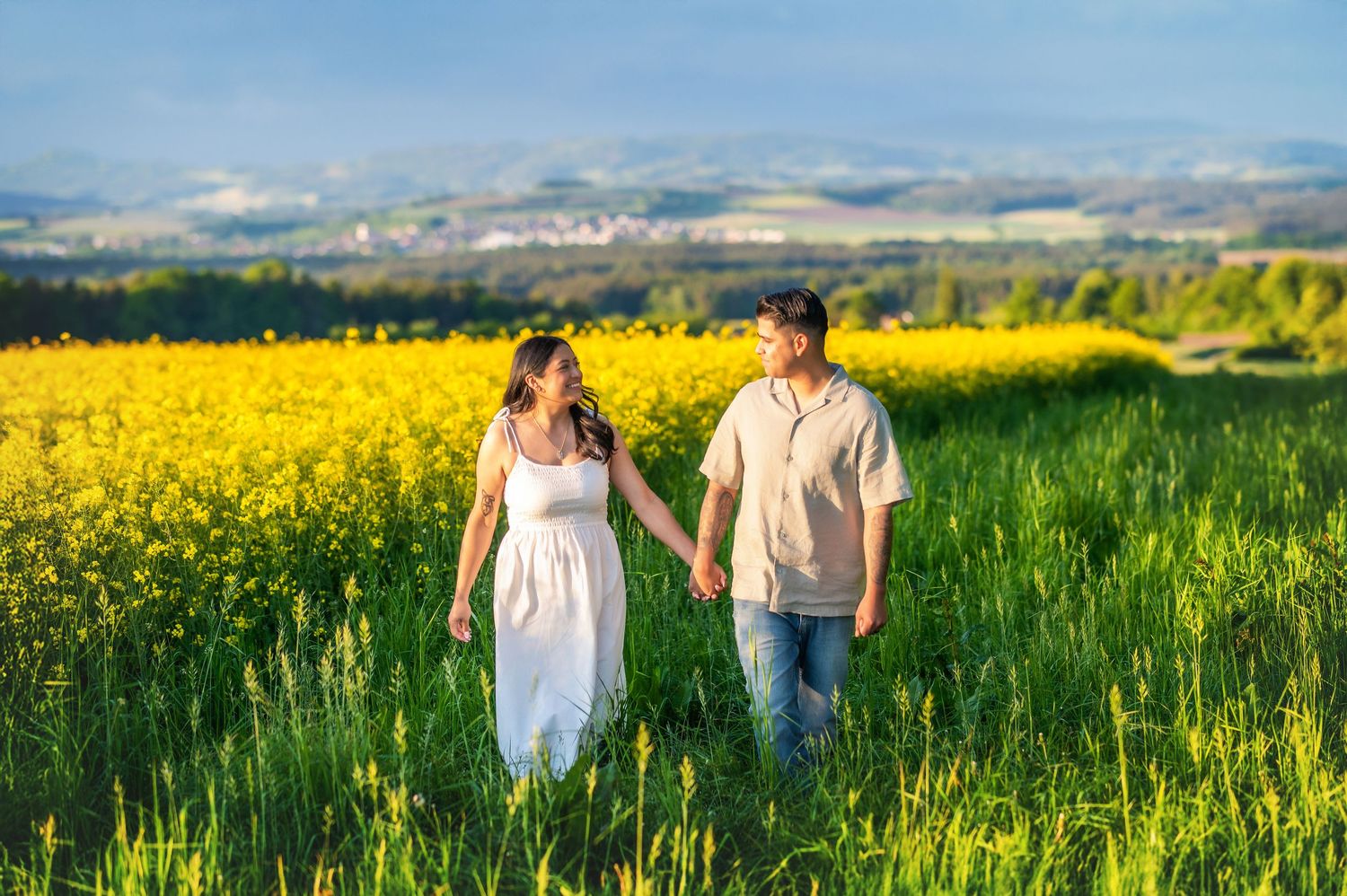 Couple walking through a lush green meadow with mountains in the background.
