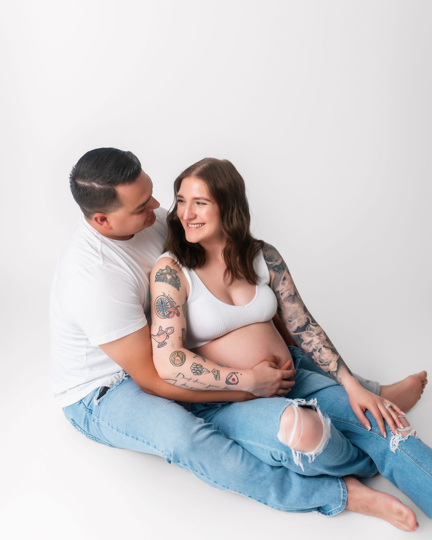 Tattooed couple shares loving moment during maternity photoshoot in studio.