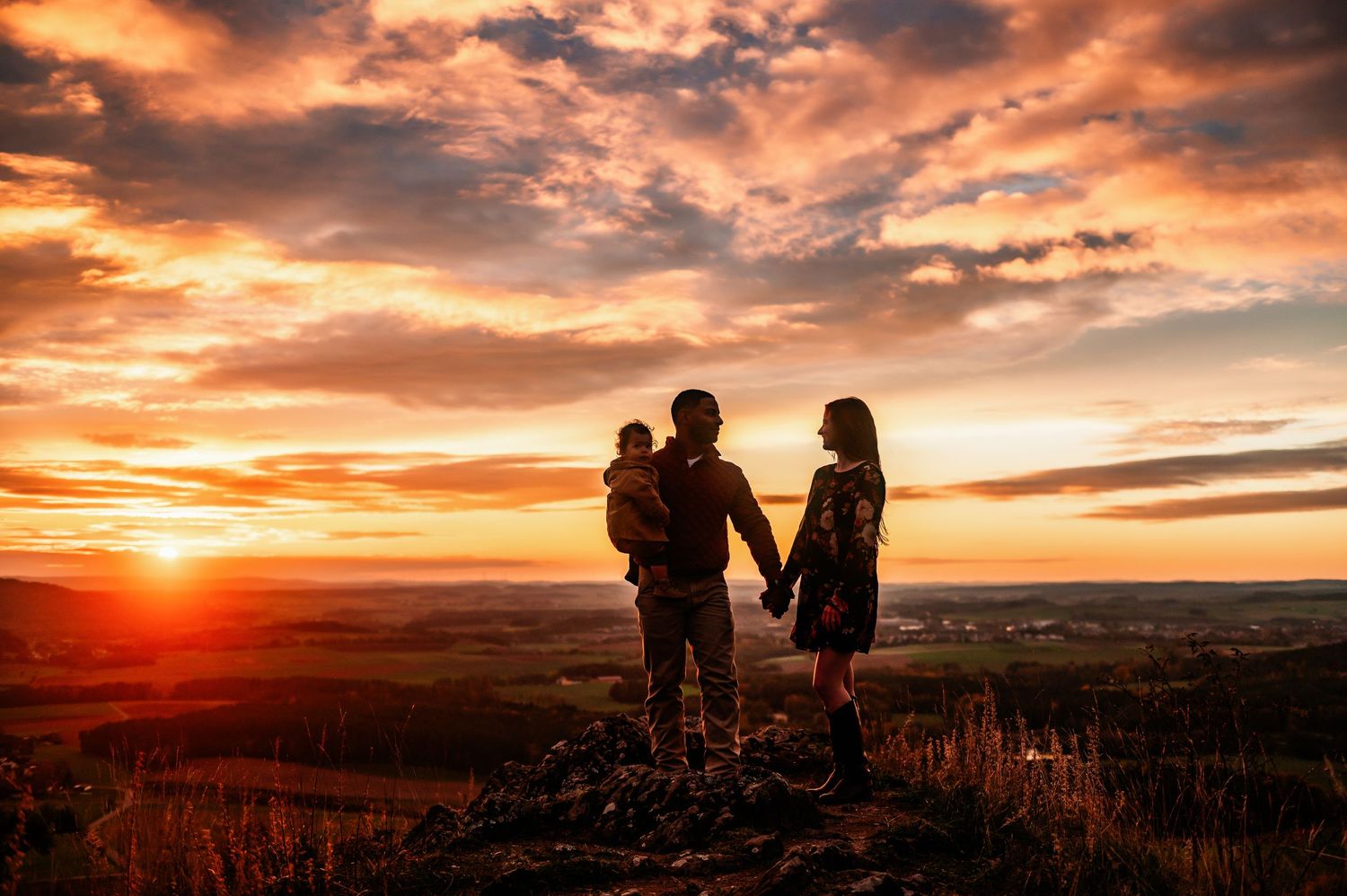 Silhouetted family stands together watching dramatic sunset over mountain landscape.
