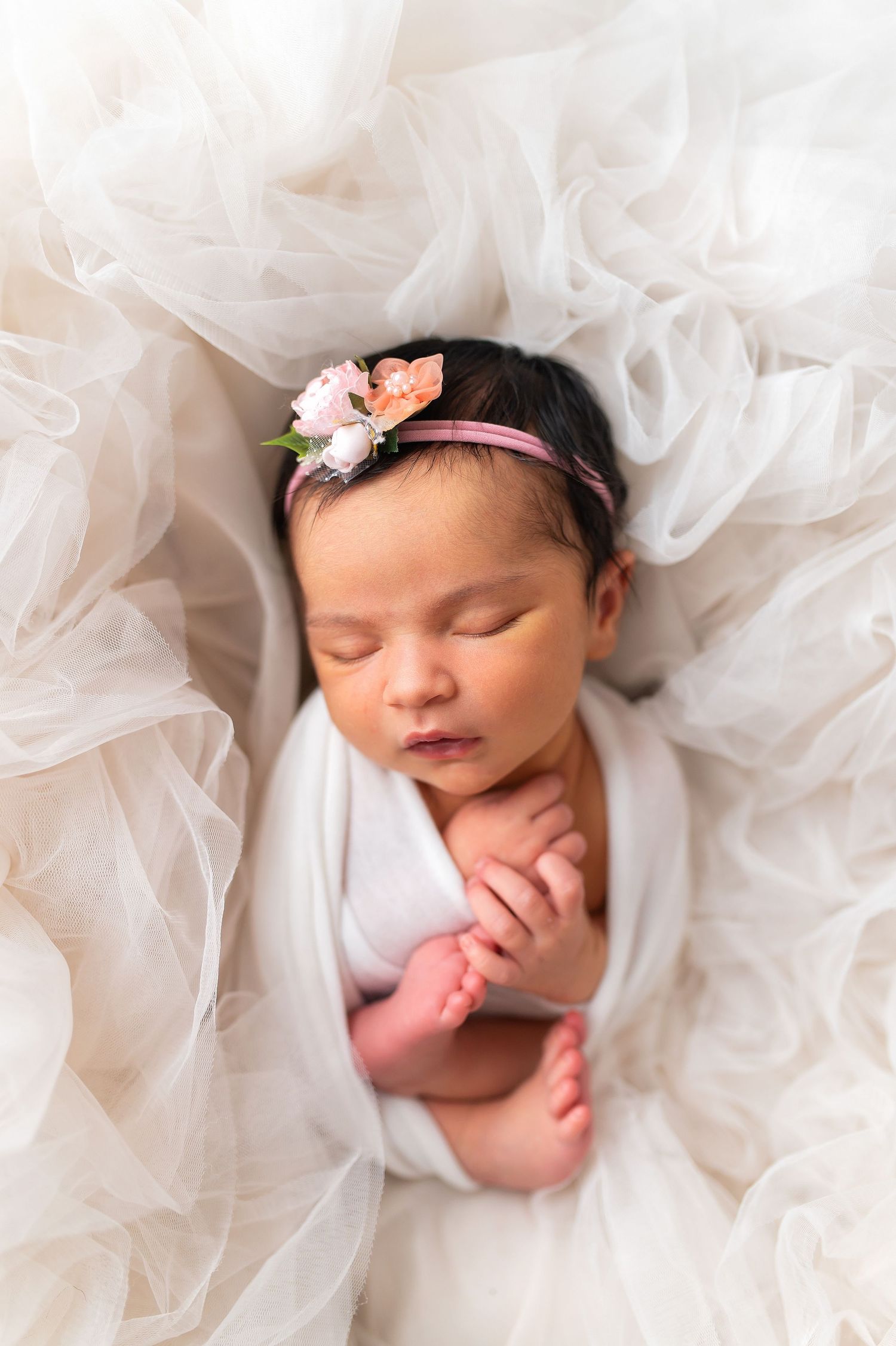 Sleeping newborn wrapped in white fabric nestled in soft tulle material.