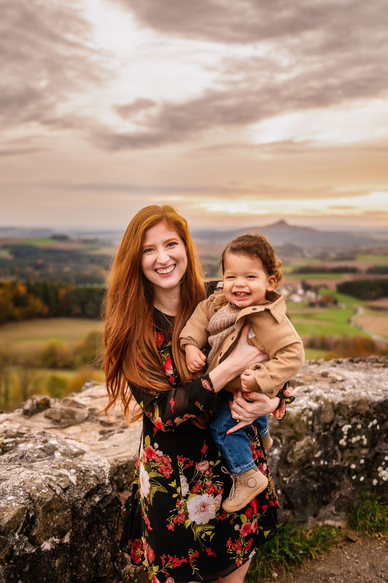 A parent and child share a joyful moment on rocky overlook during golden hour.