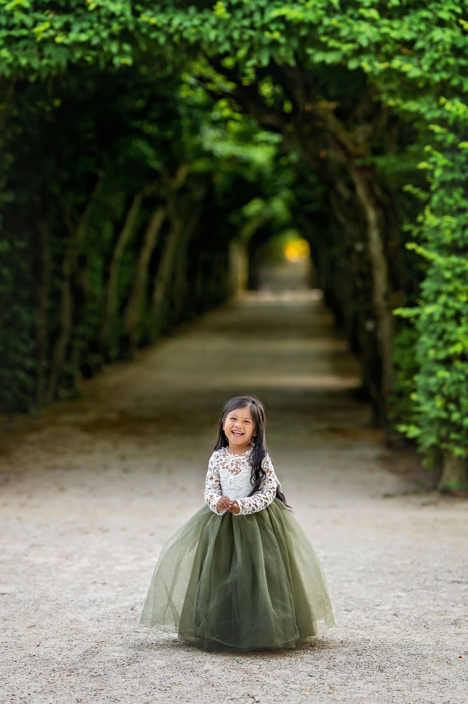 Quiet tree-lined garden path with someone wearing an elegant sage green tulle dress.