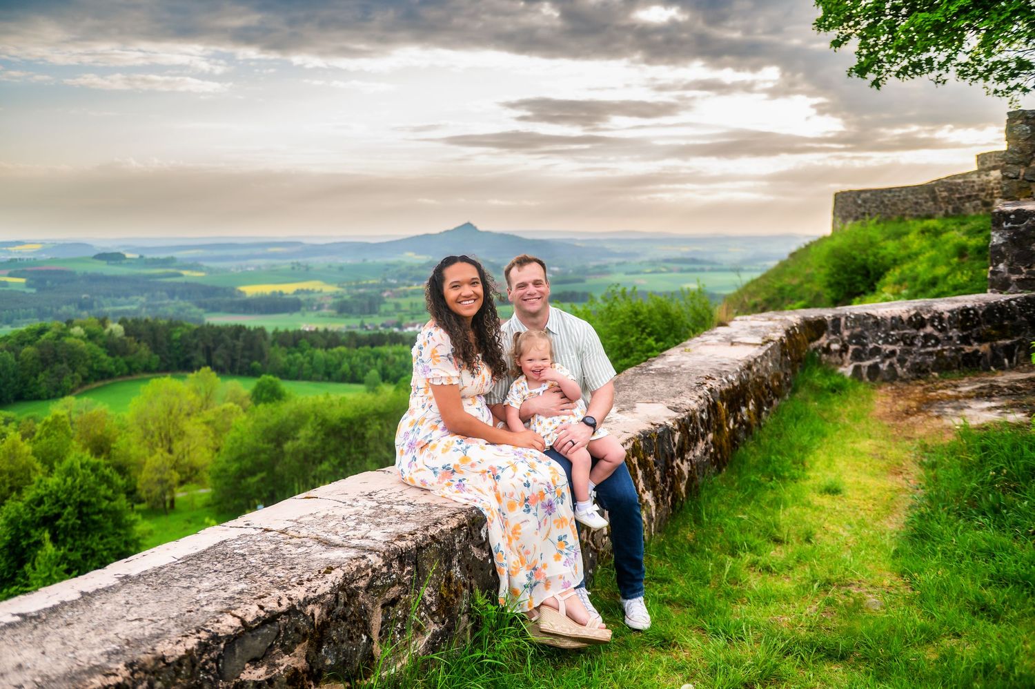 Family portrait session on a stone wall overlooking rolling green hills and countryside at sunset.