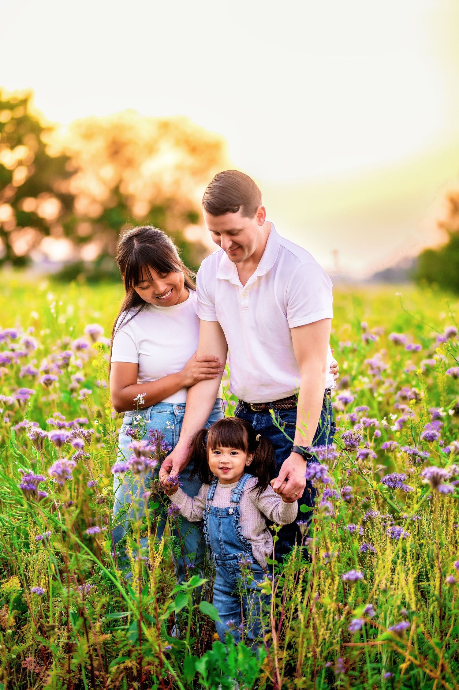 Family standing together in wildflower meadow during golden hour sunset.
