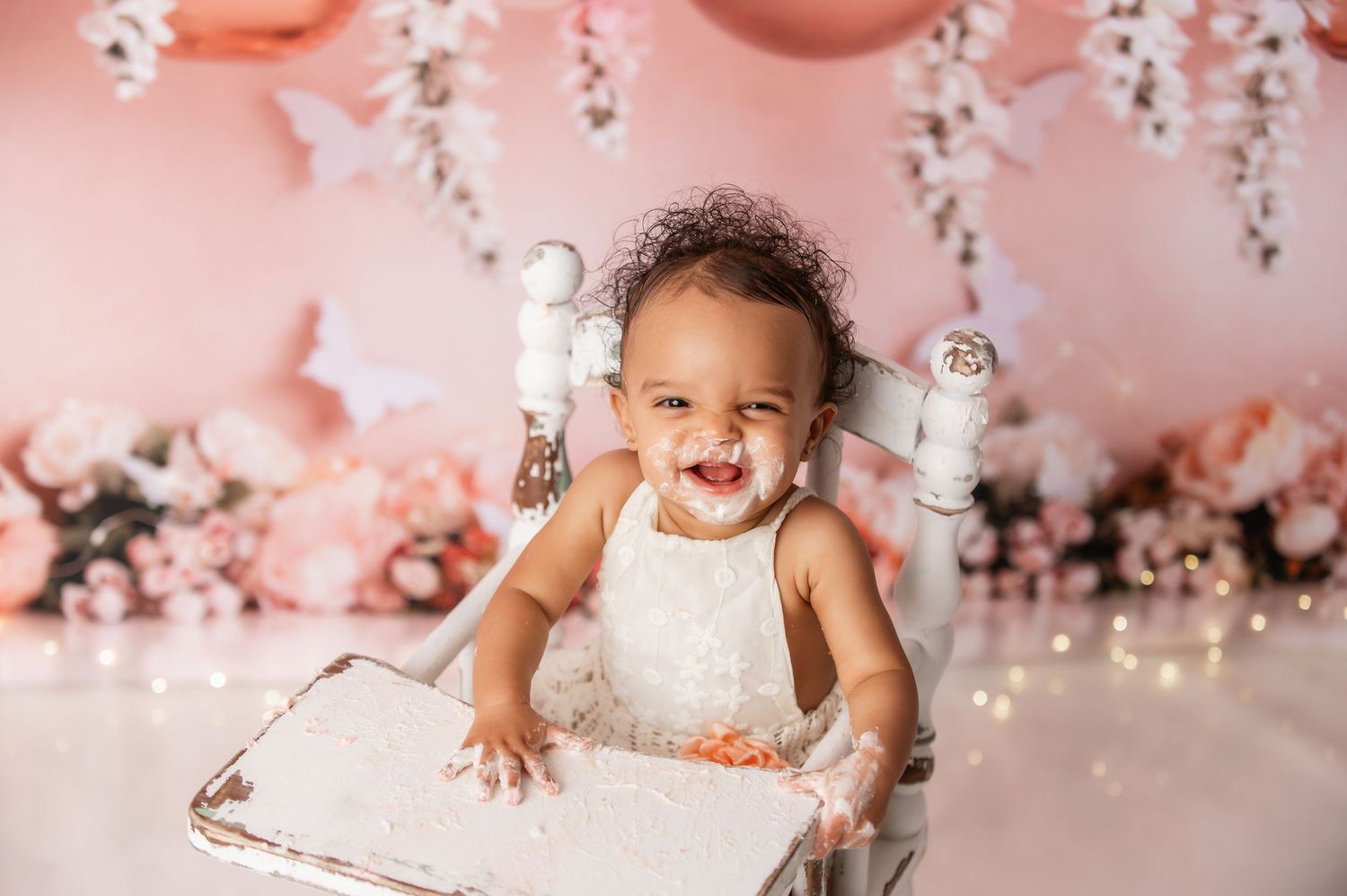 First birthday cake smash photo session with pink balloon and floral decorations.