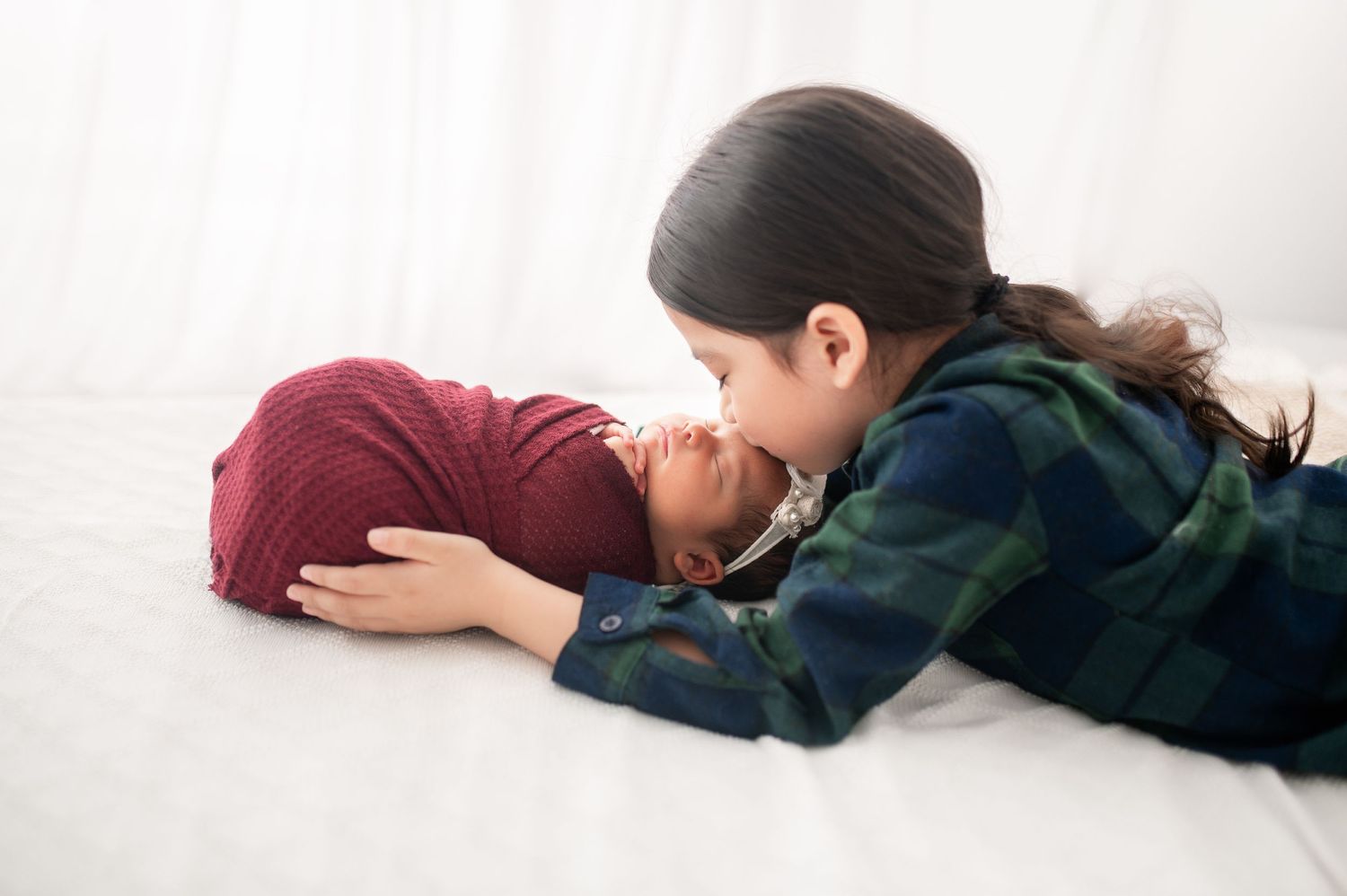 Tender moment between siblings laying on white bedding.
