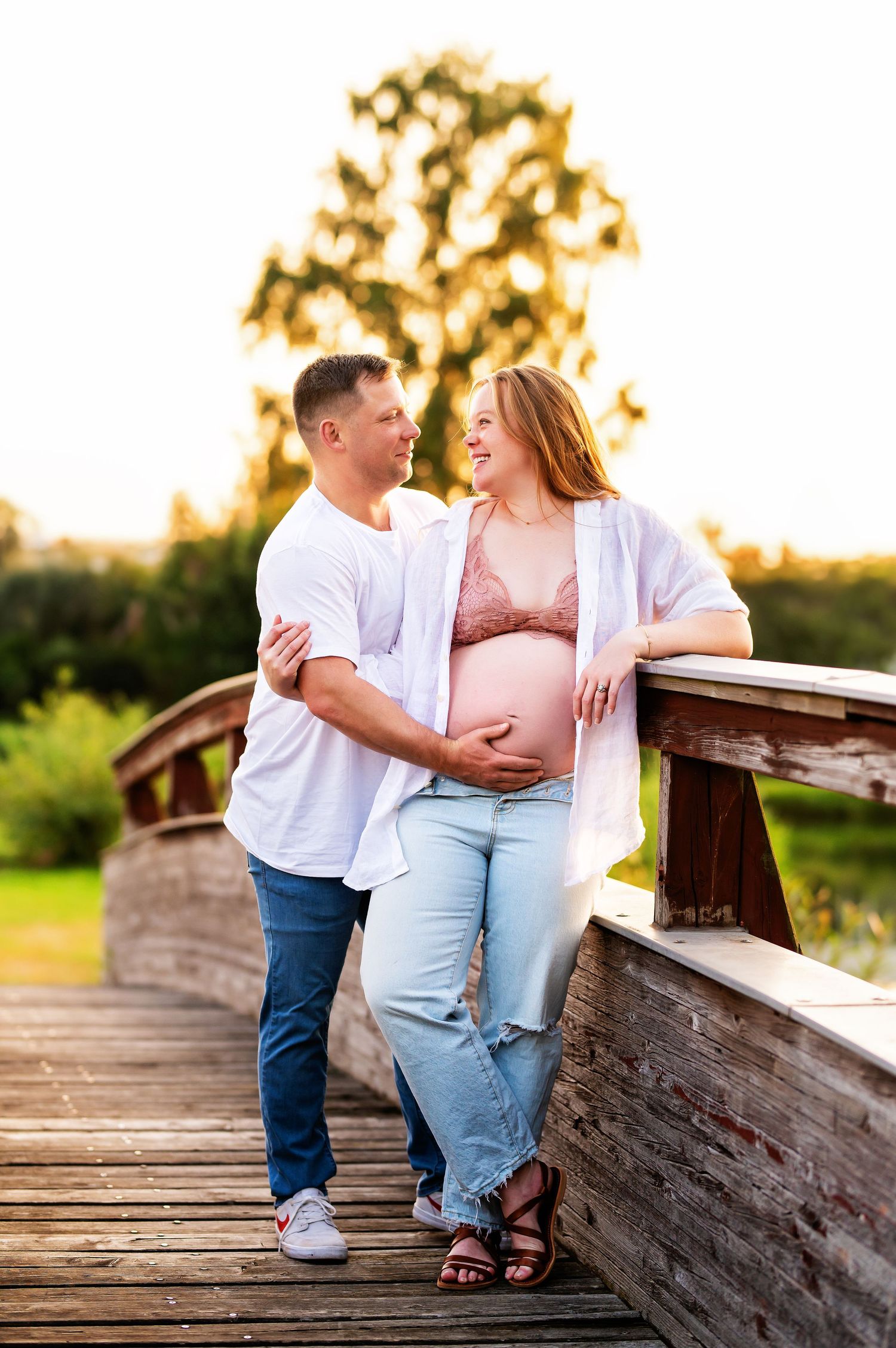 Expecting parents share intimate moment on wooden bridge during golden hour photoshoot.