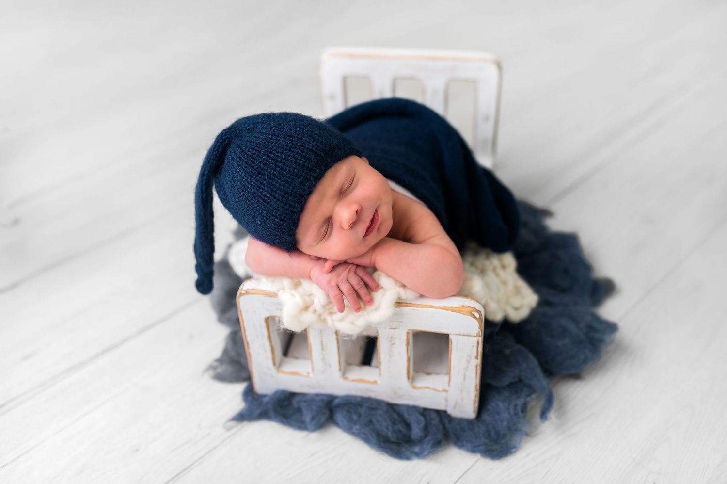 Sleeping newborn in navy hat posed on decorative white blocks with blue fabric.