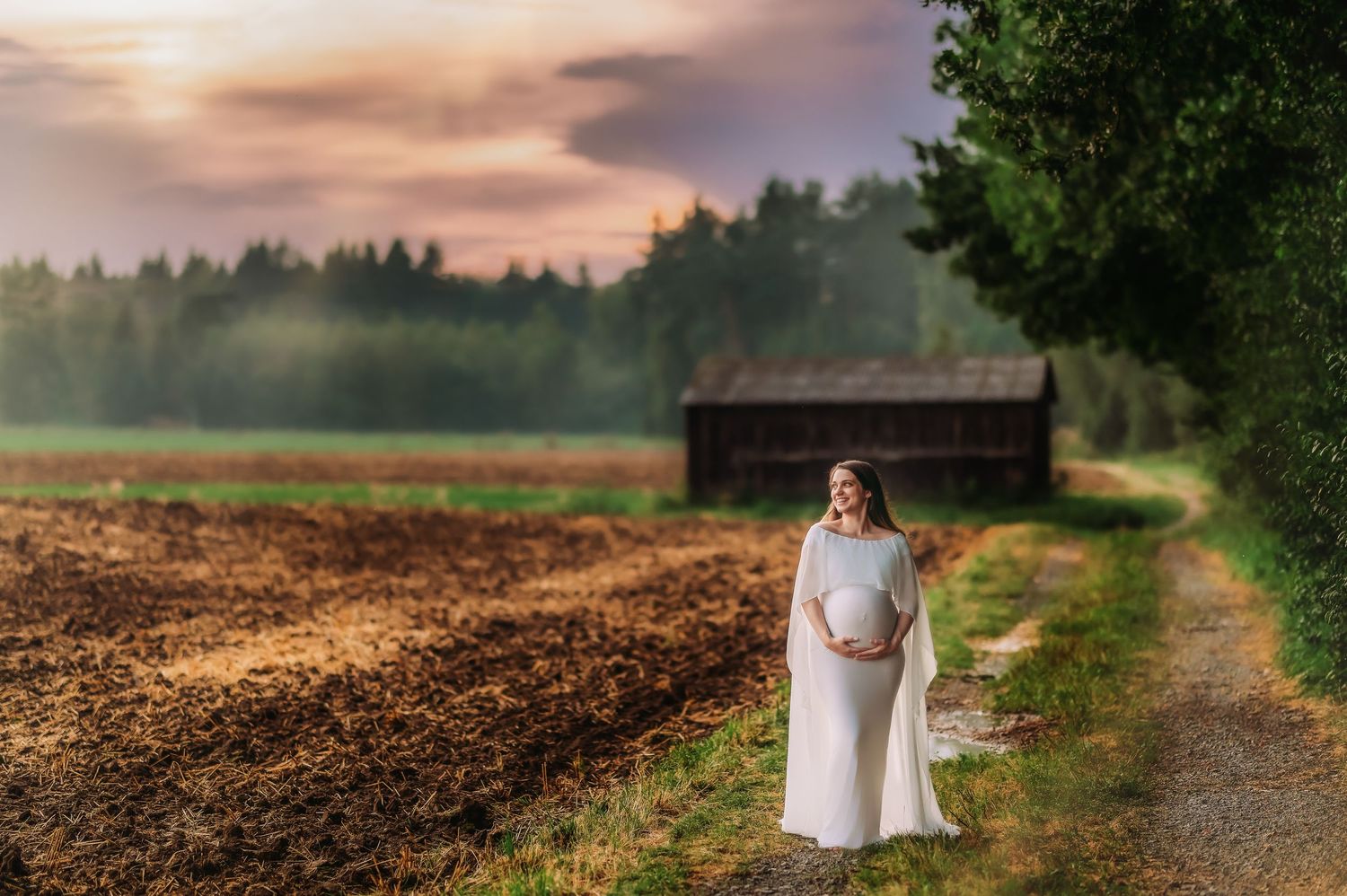 Dreamy countryside maternity session at dusk with rustic barn in background.