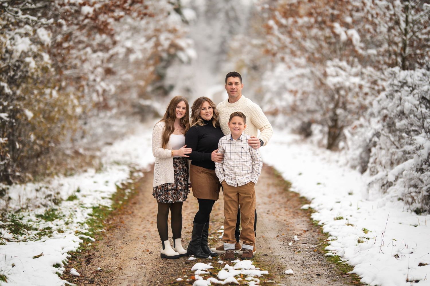 A winter family portrait session on a snowy path surrounded by frosted trees.