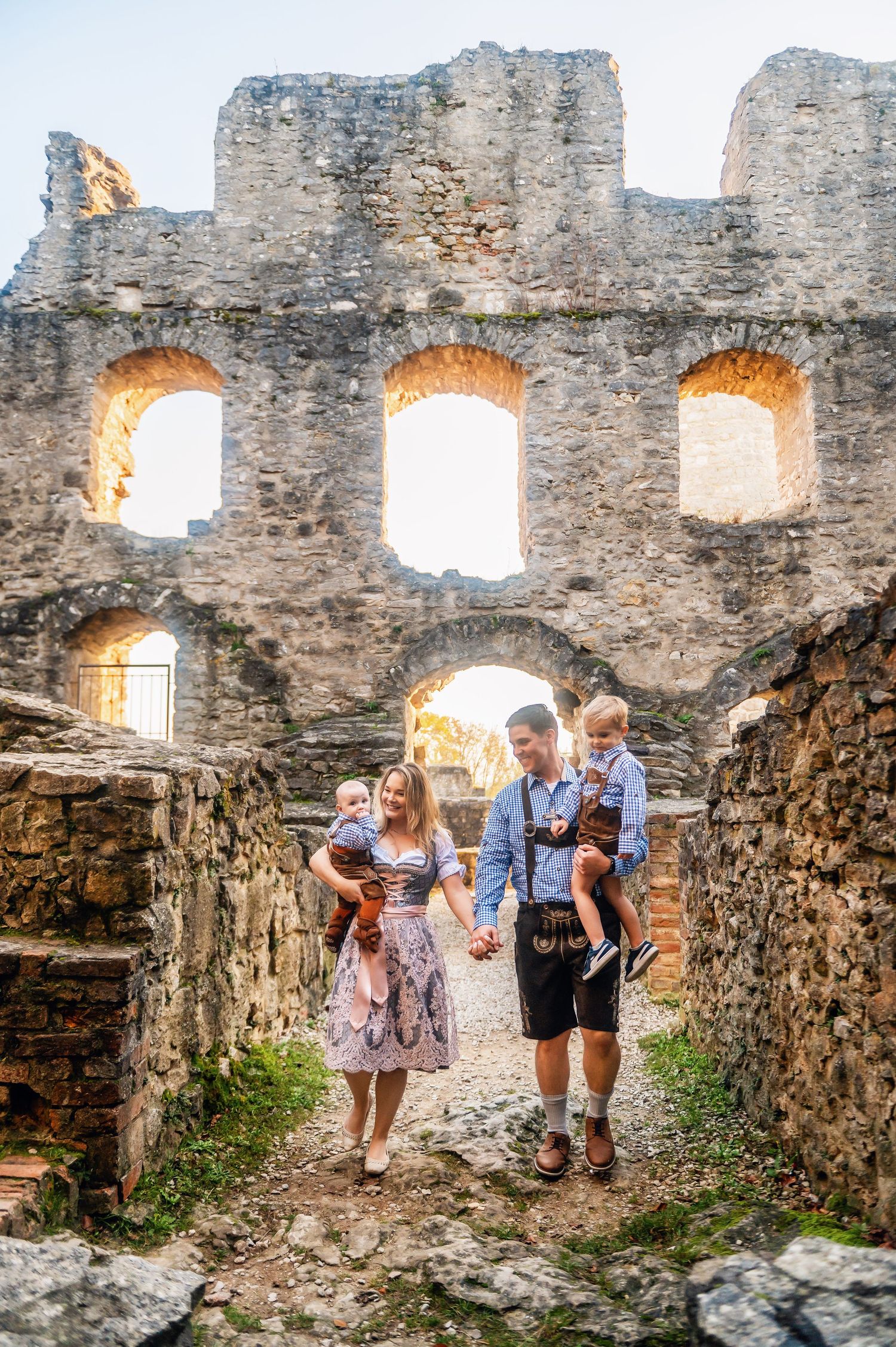 A family explores ancient castle ruins with sunlit stone arches and windows.
