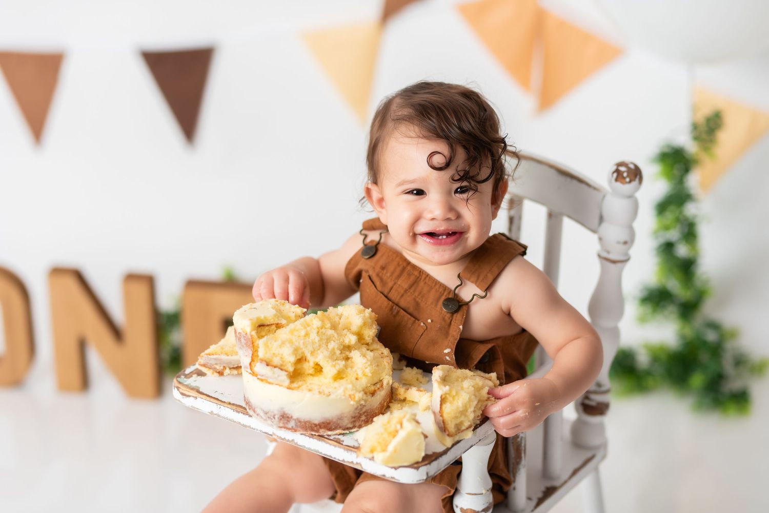 Baby smashing and enjoying cake during festive first birthday celebration with orange bunting decorations.