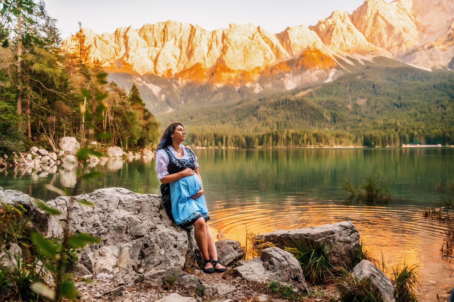 Golden sunlight illuminates the majestic peaks around Lake Eibsee in Bavaria while a person sits peacefully on a rocky shore.