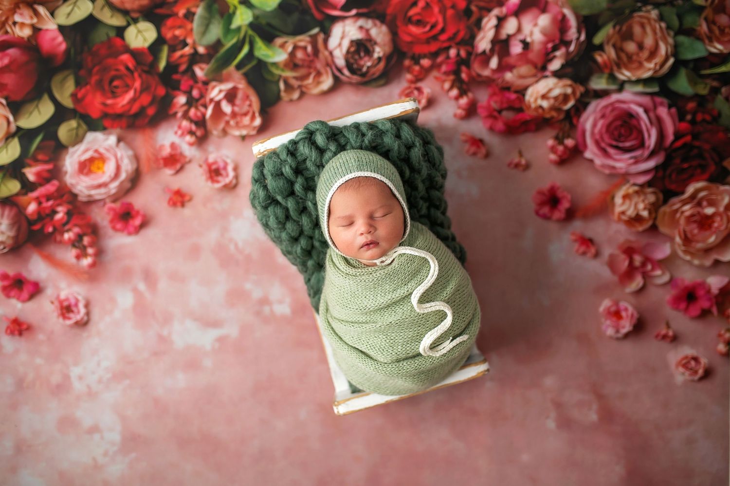 Sleeping newborn nestled among vibrant red and pink roses in artistic portrait.