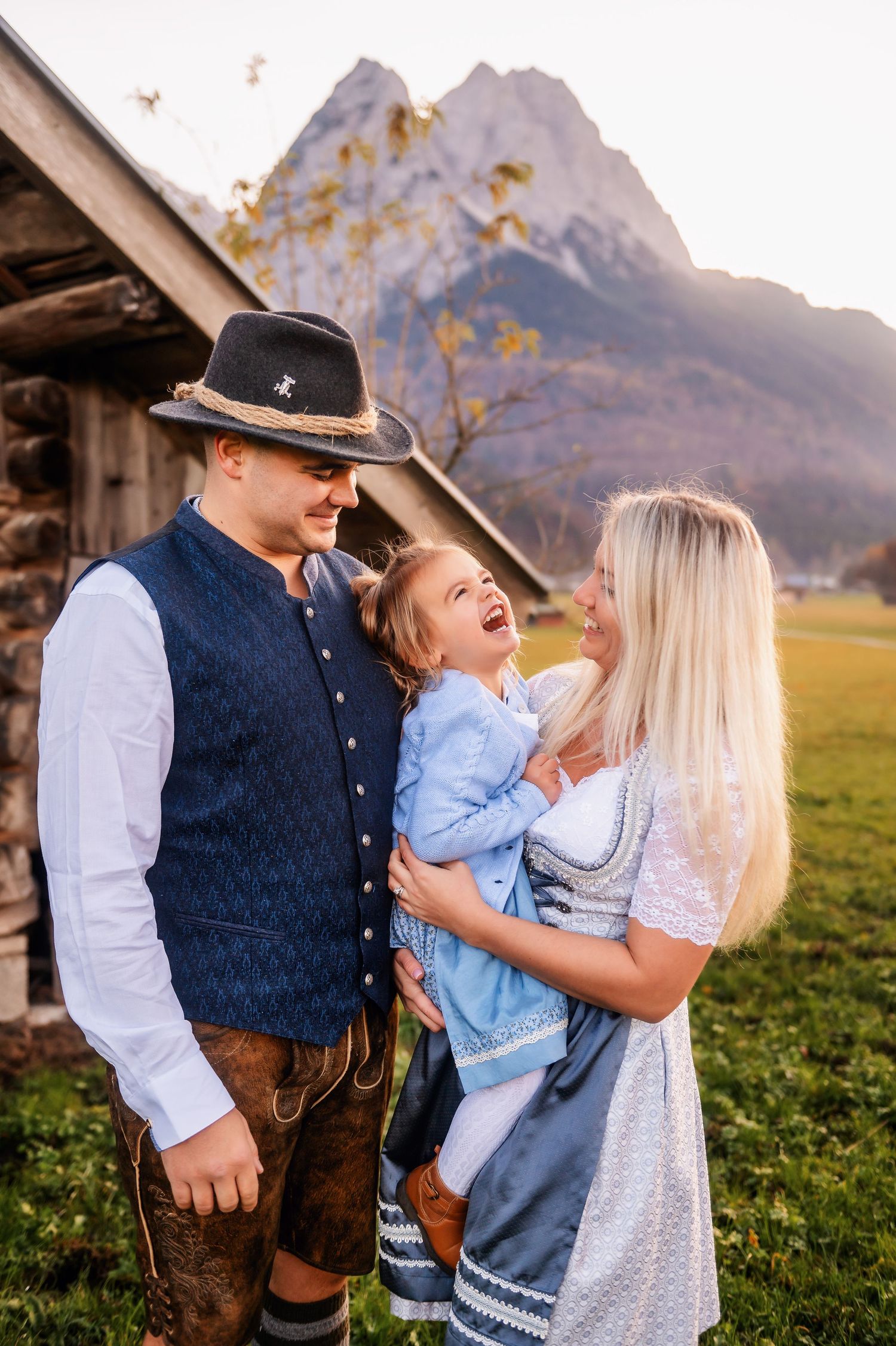 Traditional Bavarian family laughing together in front of mountain landscape during golden sunset in Alps.