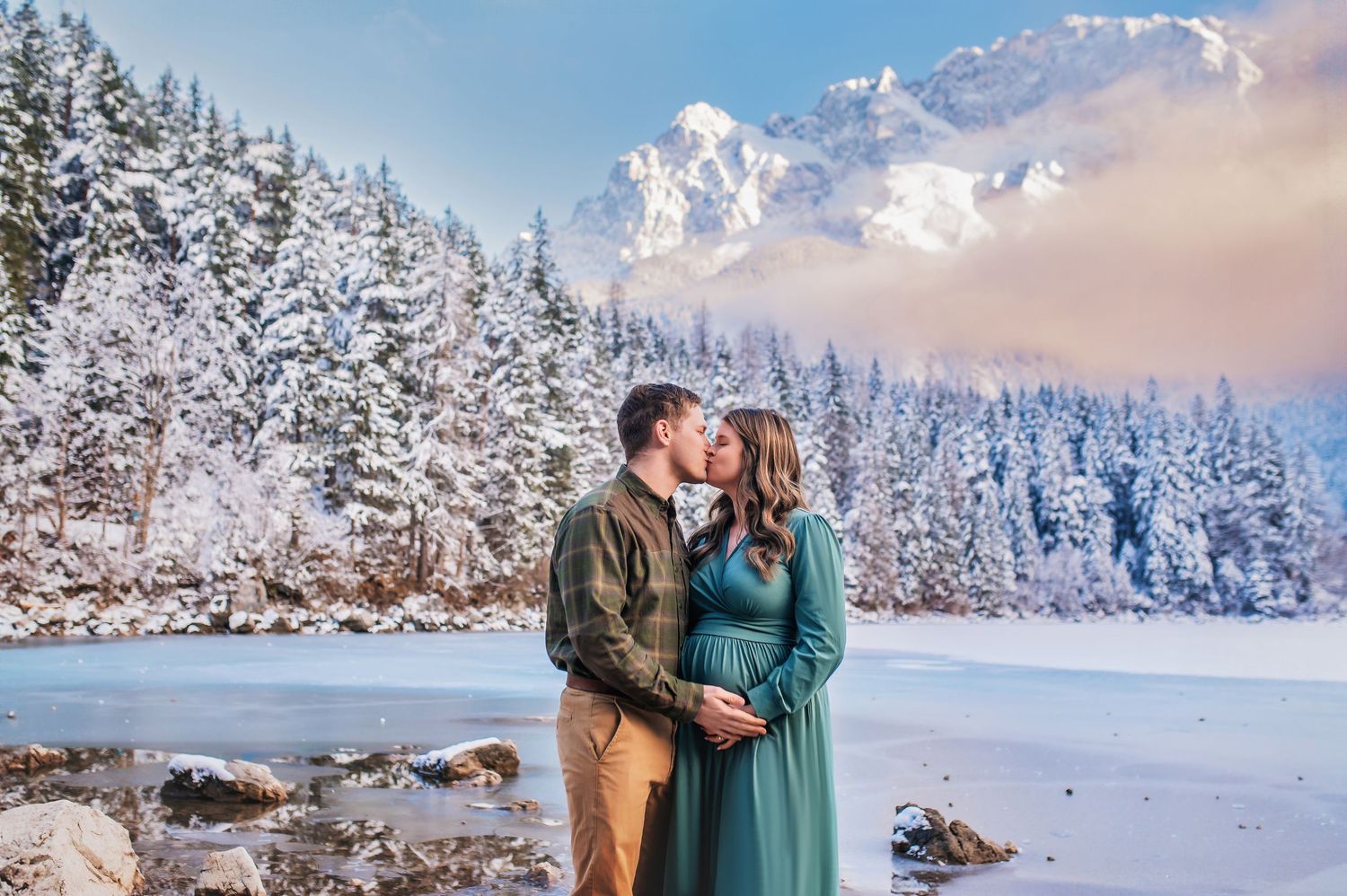 A romantic winter scene with a couple embracing by a frozen lake surrounded by snow-covered pine trees and mountains.