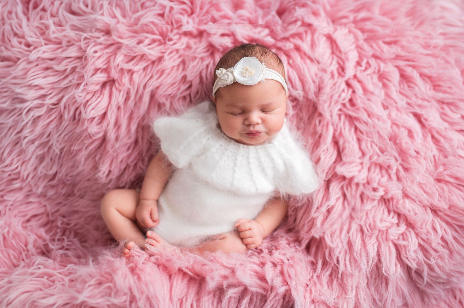 Newborn baby sleeping peacefully on pink fluffy blanket in studio portrait.