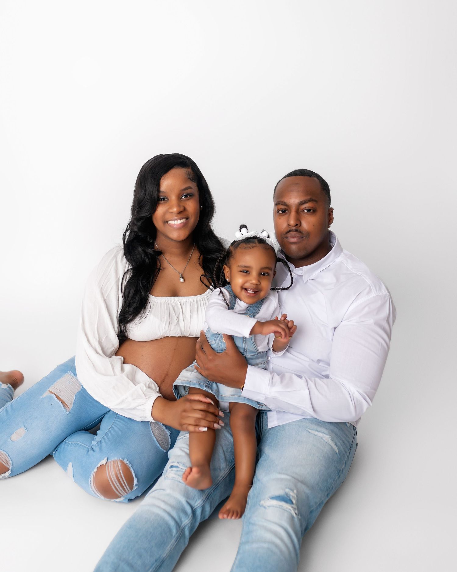 Candid family maternity photo with parents and toddler in casual white and denim.
