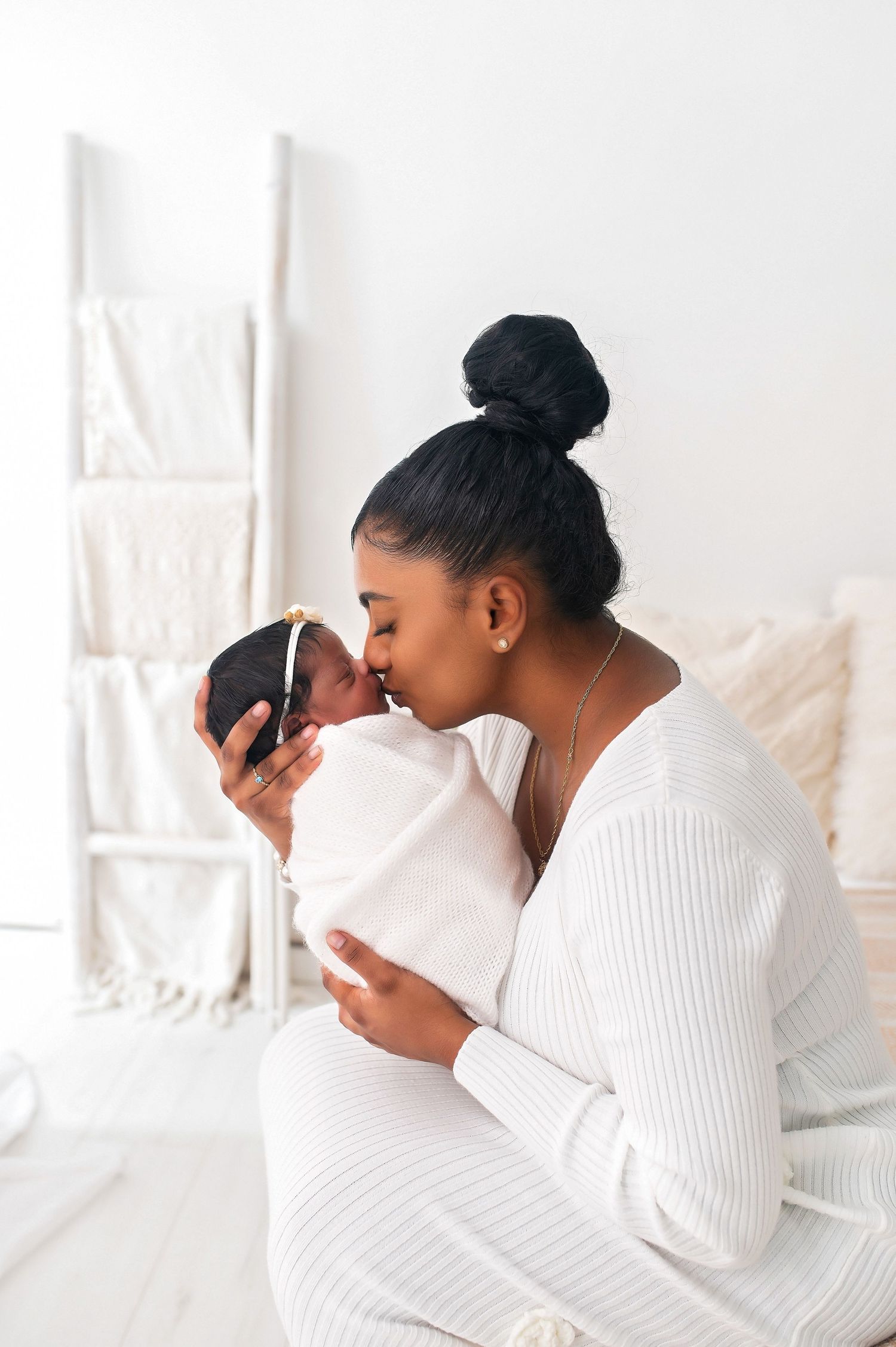 A tender family moment on a white bed with soft natural lighting and cream-colored bedding.