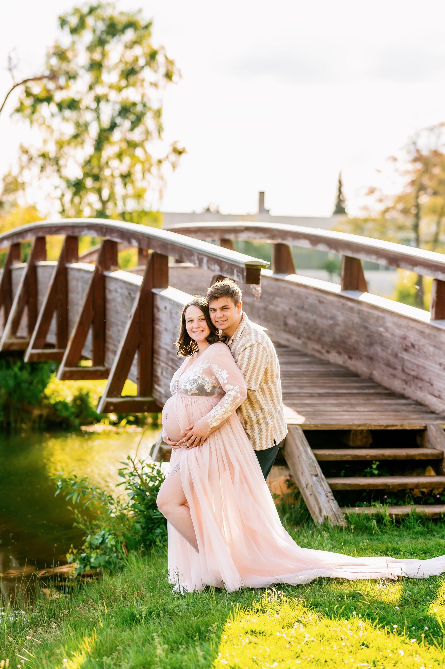 Couple sharing intimate moment on wooden bridge during sunset maternity session.